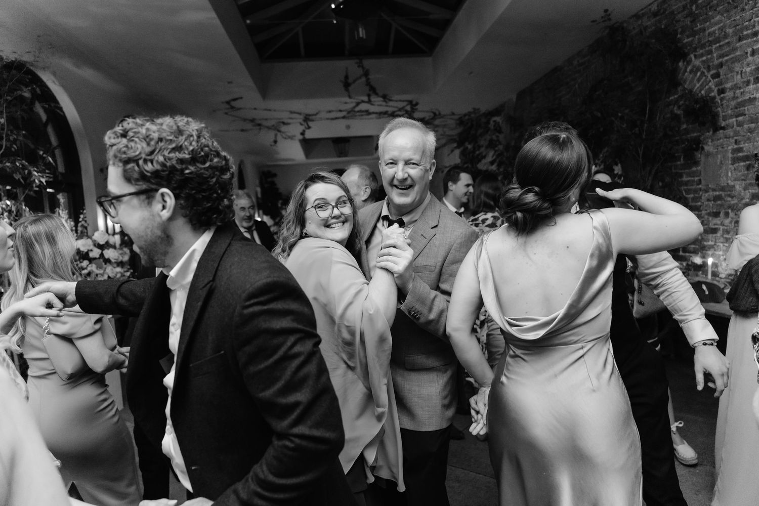 Black and white photo of wedding guests laughing and dancing together at a reception celebration.