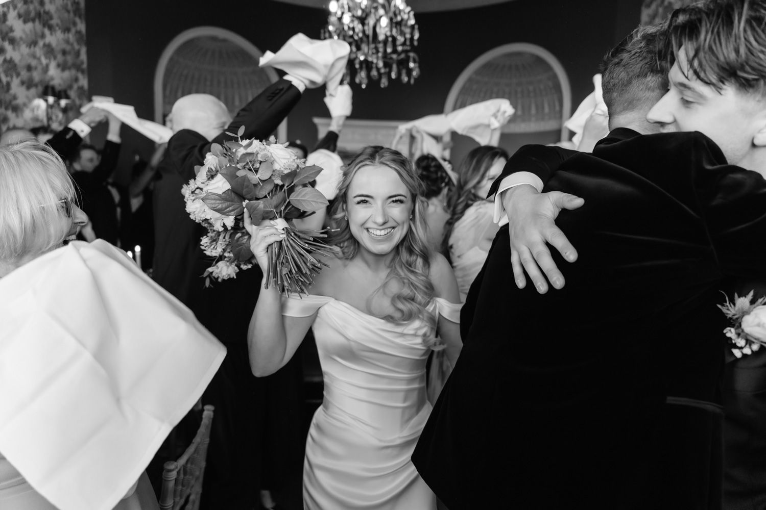 Joyful bride dancing with guests waving napkins during a lively wedding reception celebration.