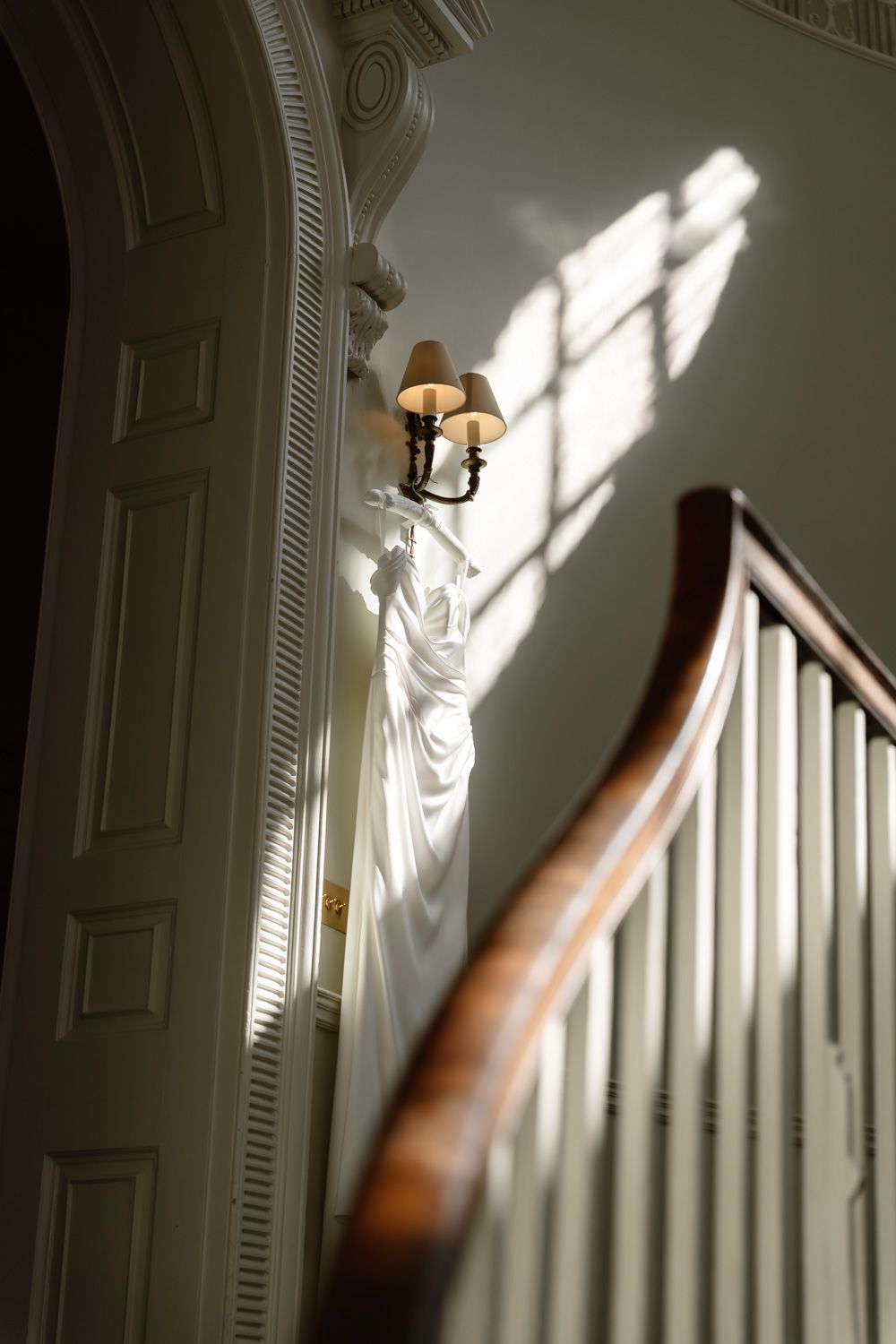 Wedding dress hanging on wall sconce beside elegant staircase with beautiful natural window light.