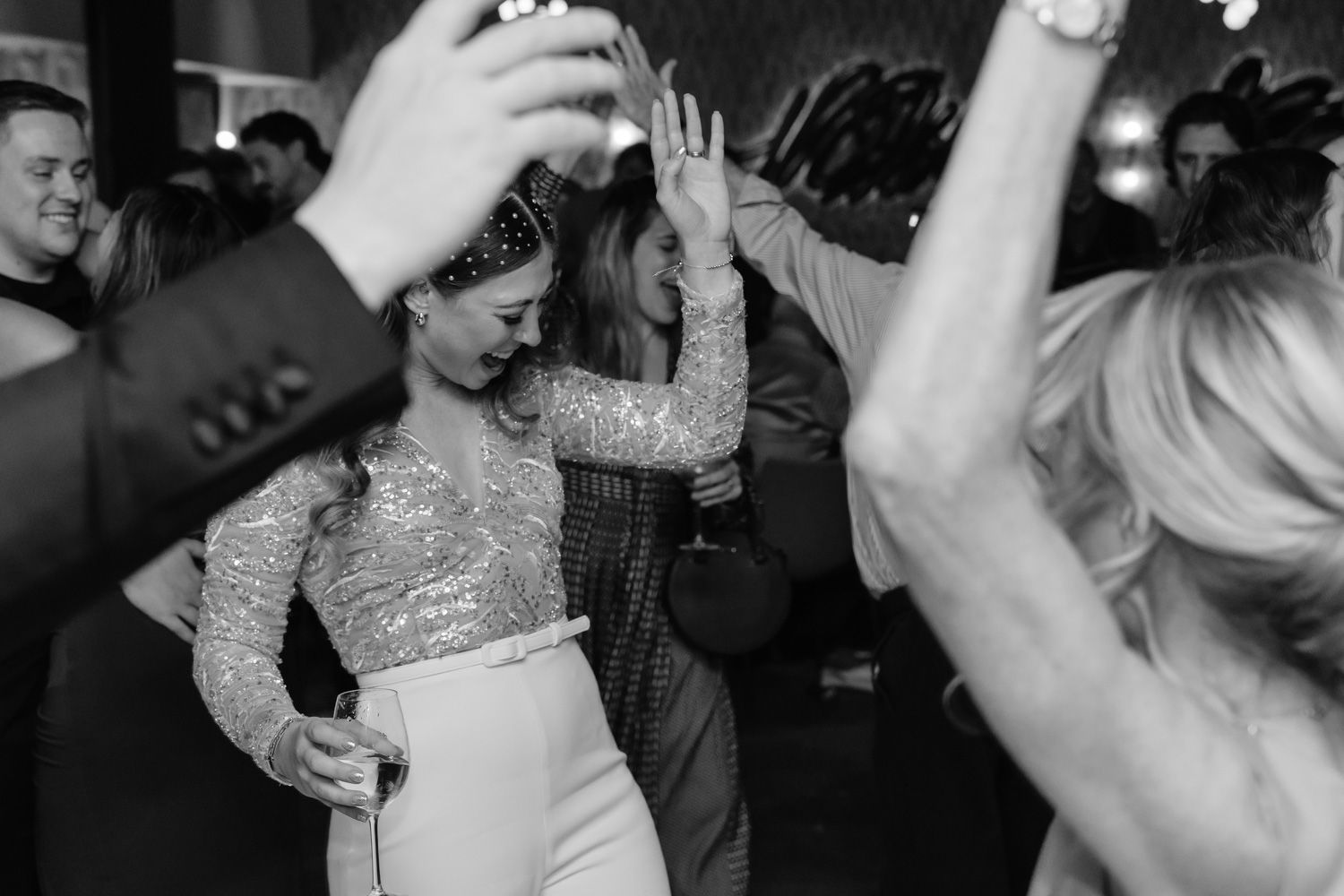 Bride dancing joyfully with guests at a lively wedding reception in black and white.