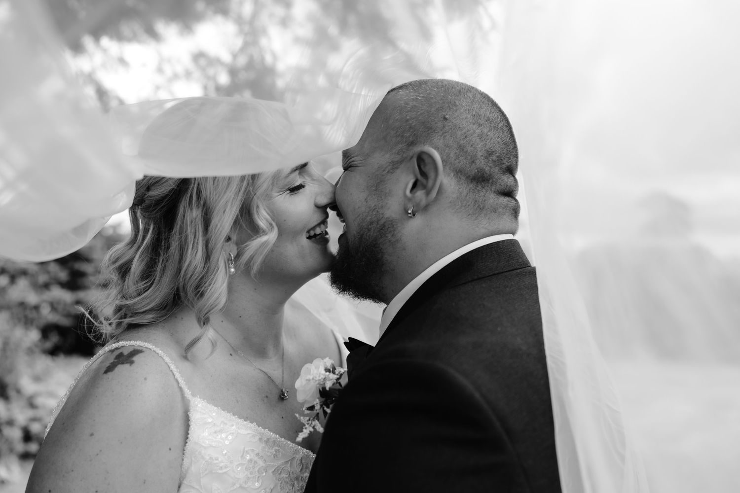 Black and white wedding photo of bride and groom sharing a romantic almost-kiss, veil flowing around them.