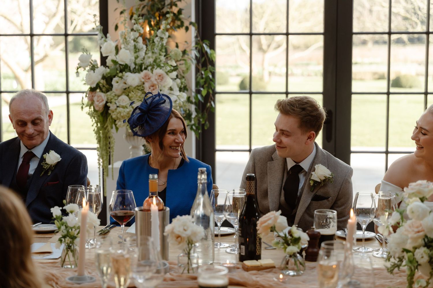 Wedding guests laughing and smiling at a beautifully decorated reception table with white floral arrangements.