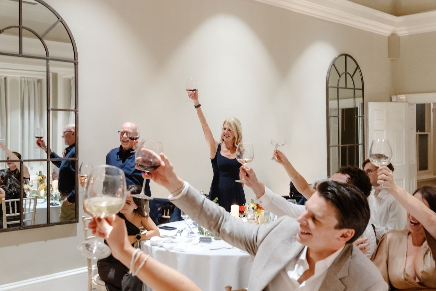 Wedding guests raising glasses in a toast in a bright elegant reception room.