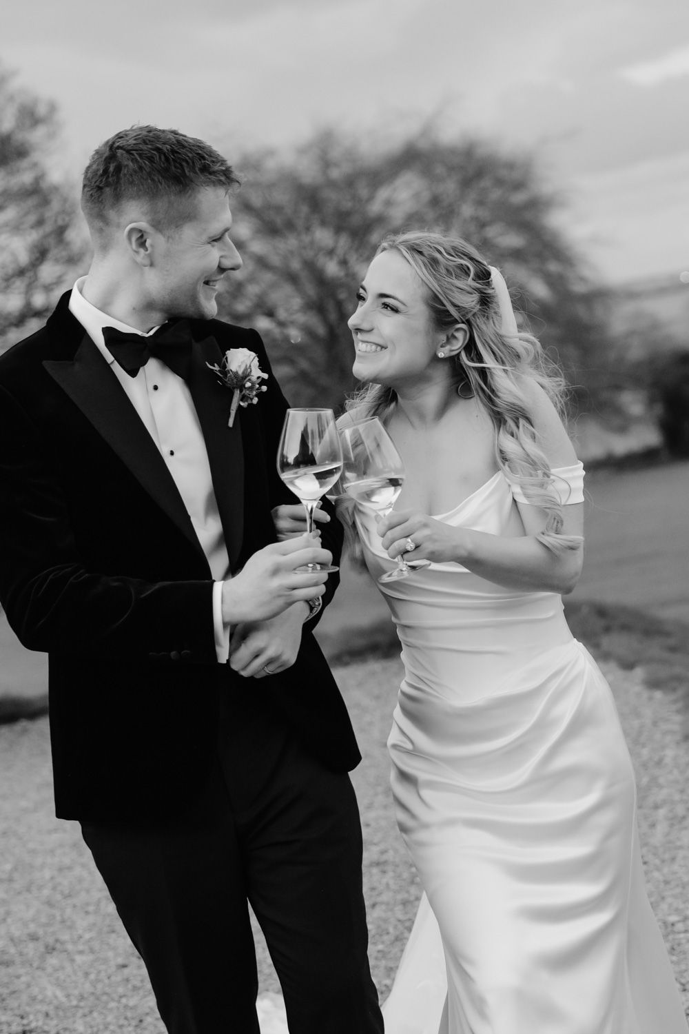 Bride and groom toast with wine glasses smiling at each other in black and white.