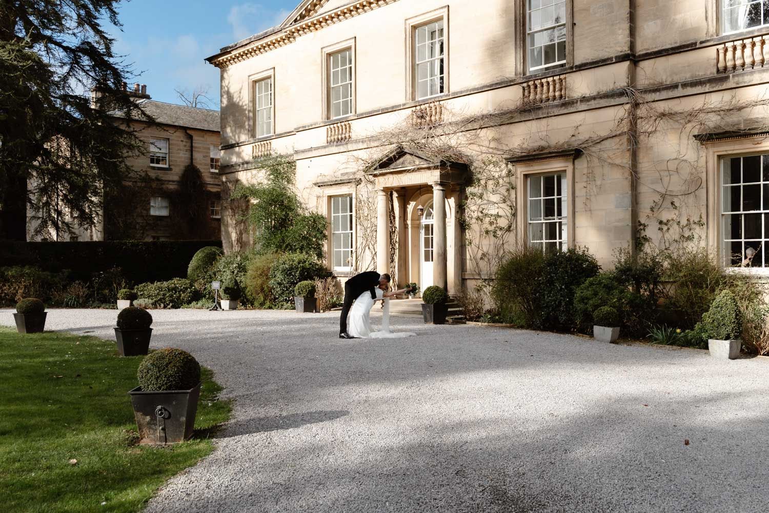 Bride and groom sharing a romantic dip in front of a grand estate.