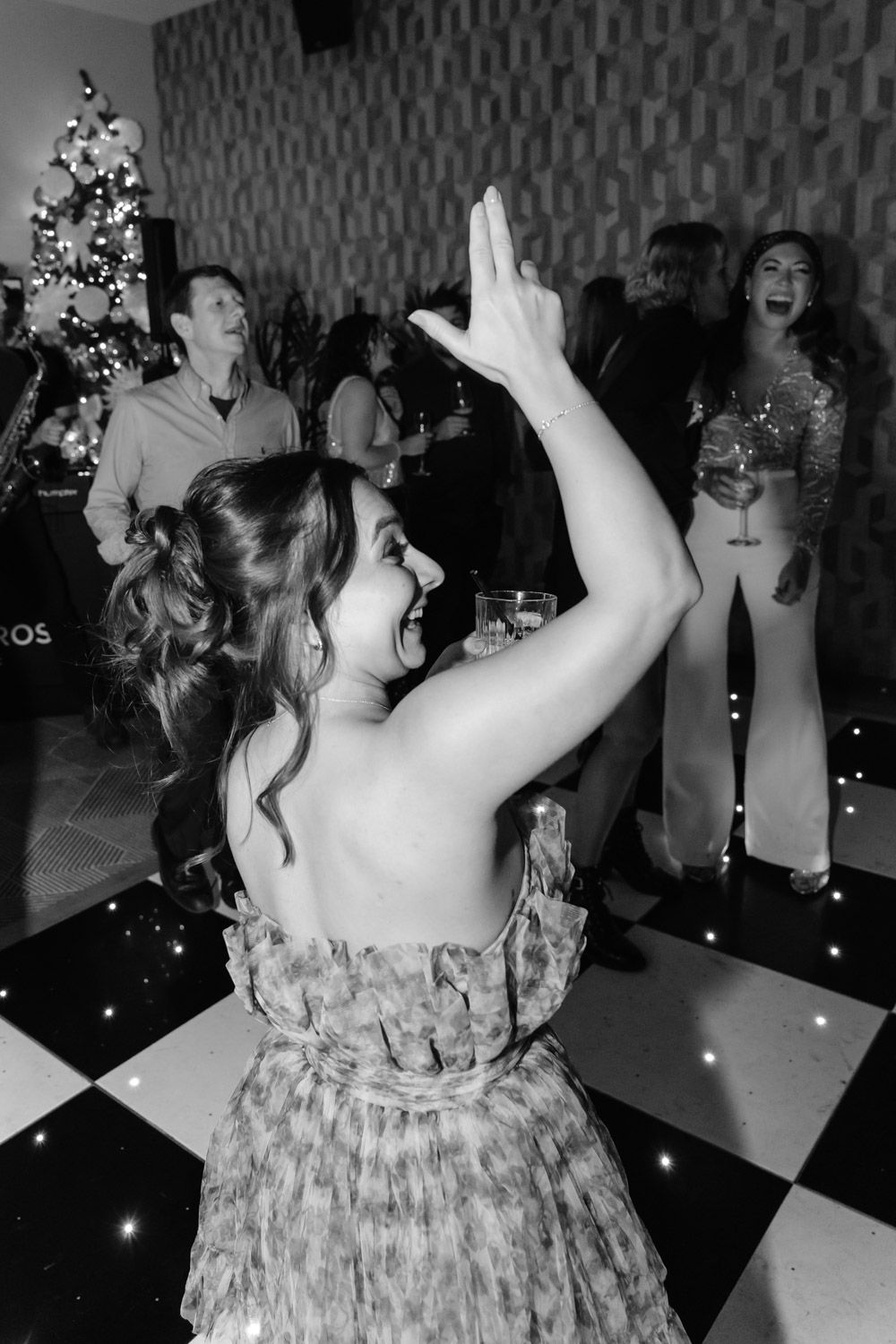 Black and white photo of woman dancing joyfully at festive wedding reception.