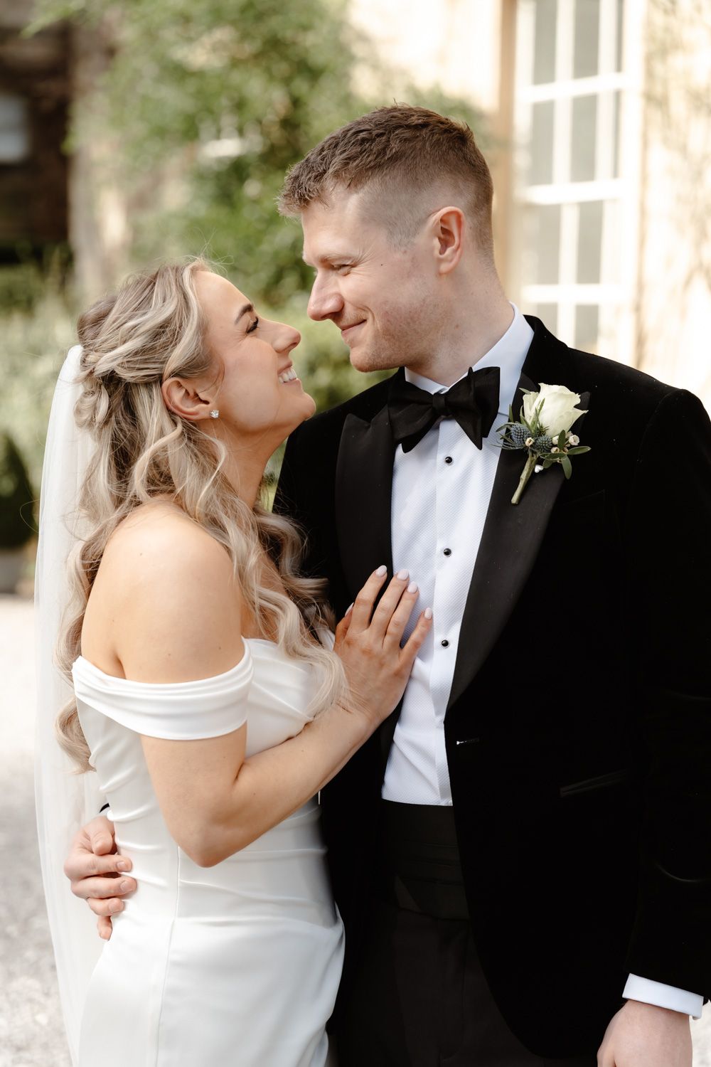 Bride and groom sharing a loving smile outside a stunning stone manor wedding venue.