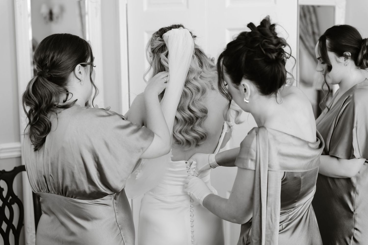 Black and white photo of bridesmaids helping bride with her wedding dress before the ceremony.