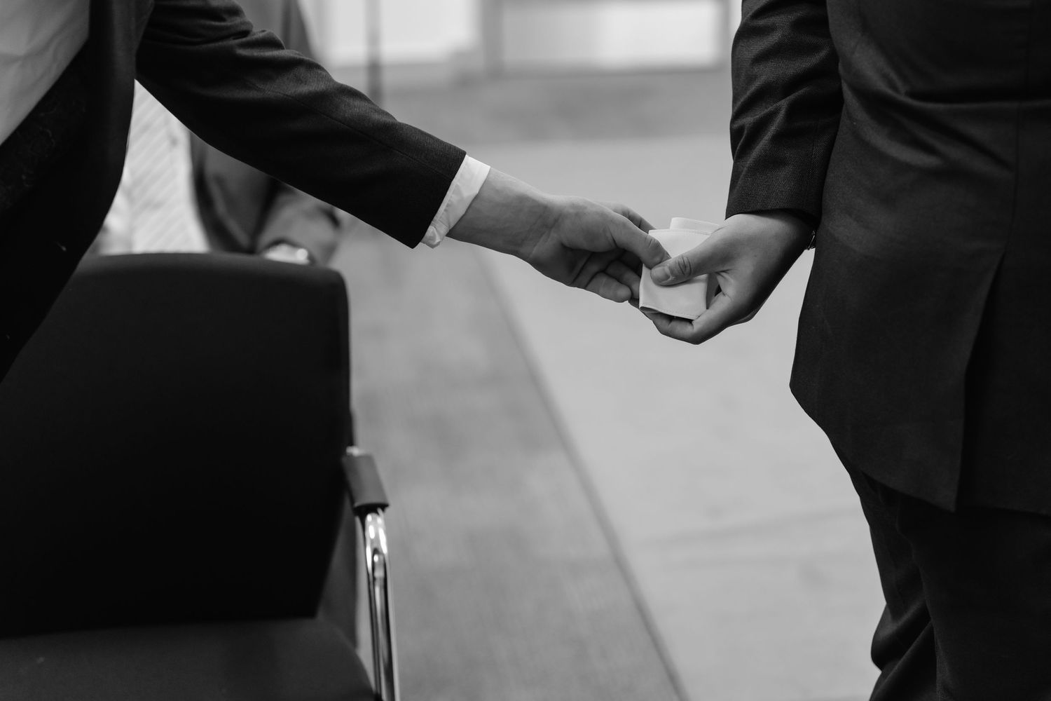 Two businessmen in suits exchanging business cards in a black and white professional setting.