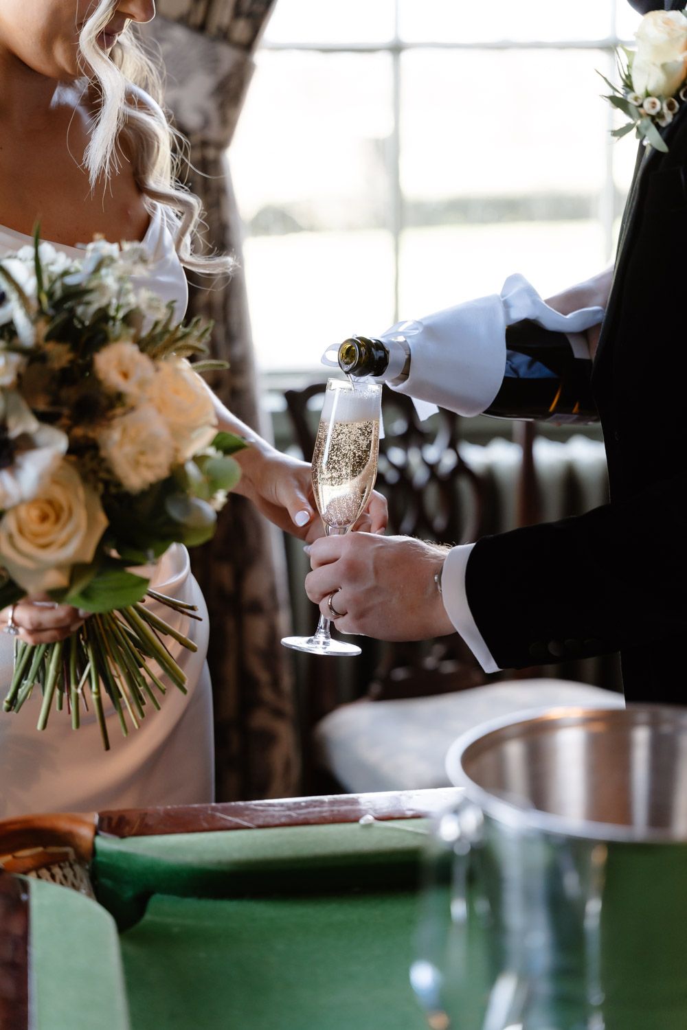 Champagne being poured into a flute held by the bride in a white gown at the wedding reception.