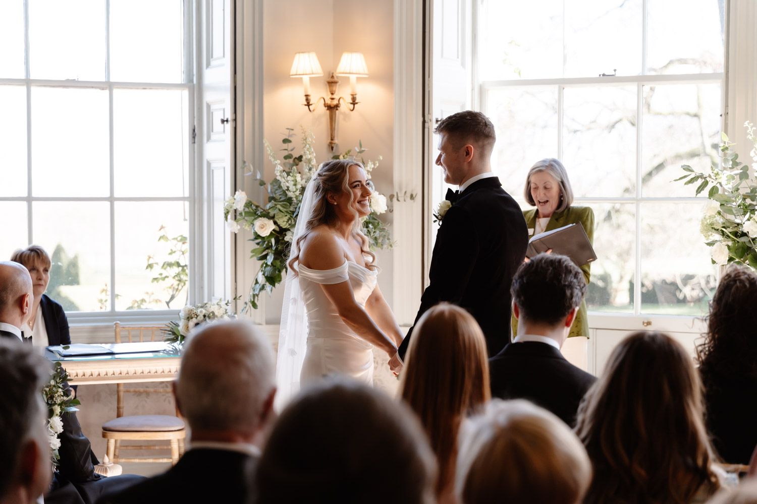 Bride and groom hold hands at the altar as female officiant reads during elegant indoor wedding ceremony.