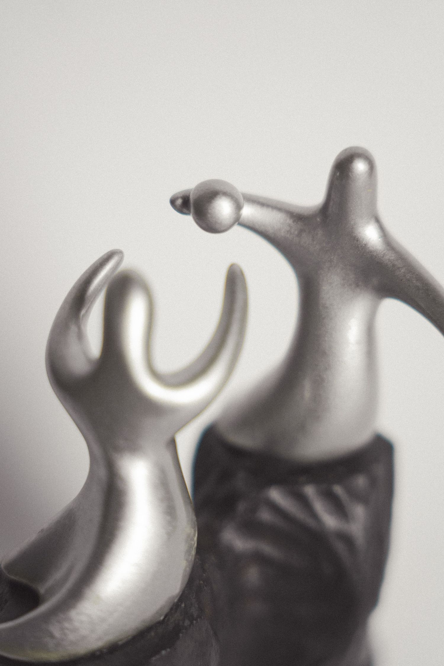 Two abstract silver metallic figurines with smooth curves posed together against a light gray background.