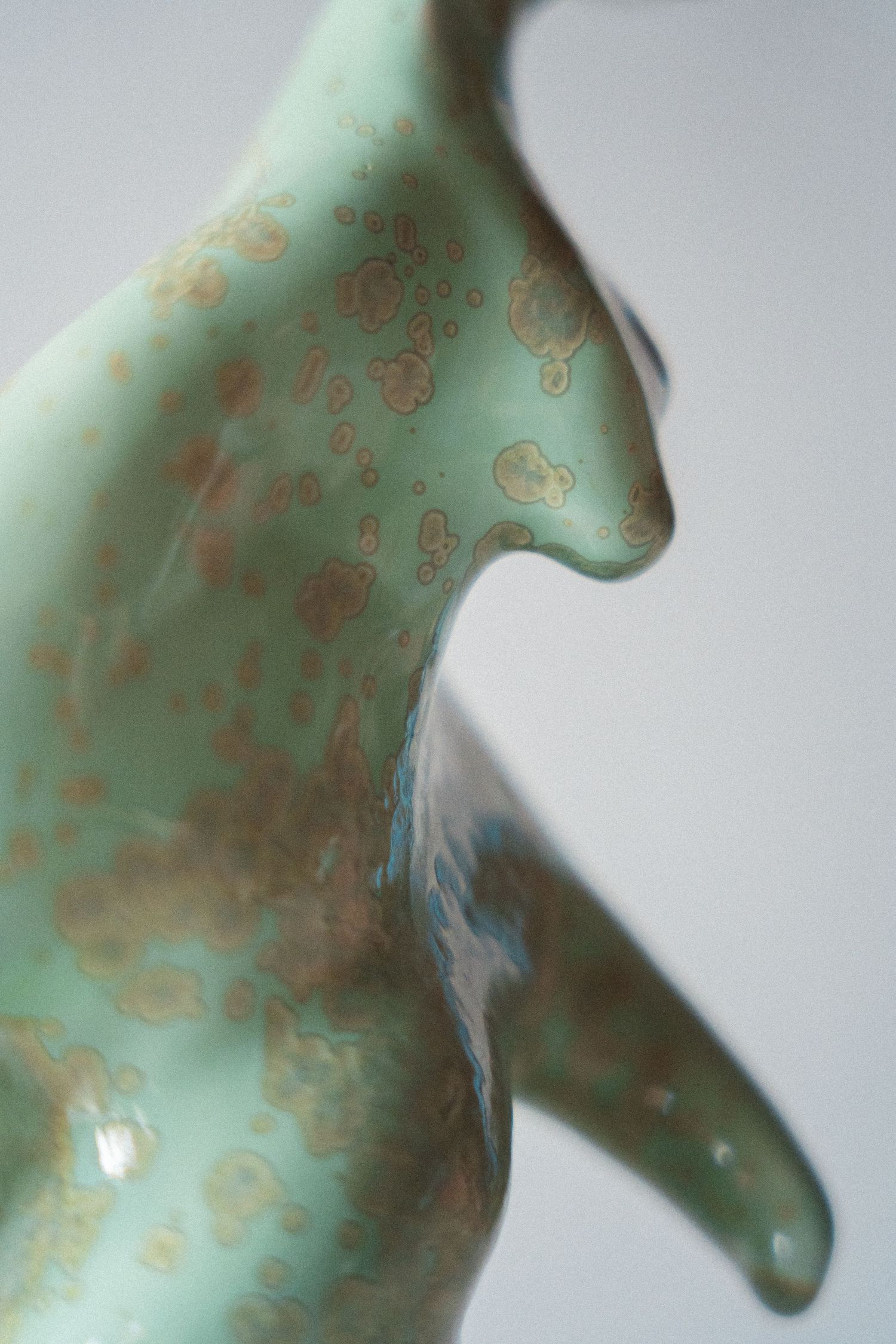 Close-up detail of a ceramic animal figurine with a speckled mint green and copper glaze finish.