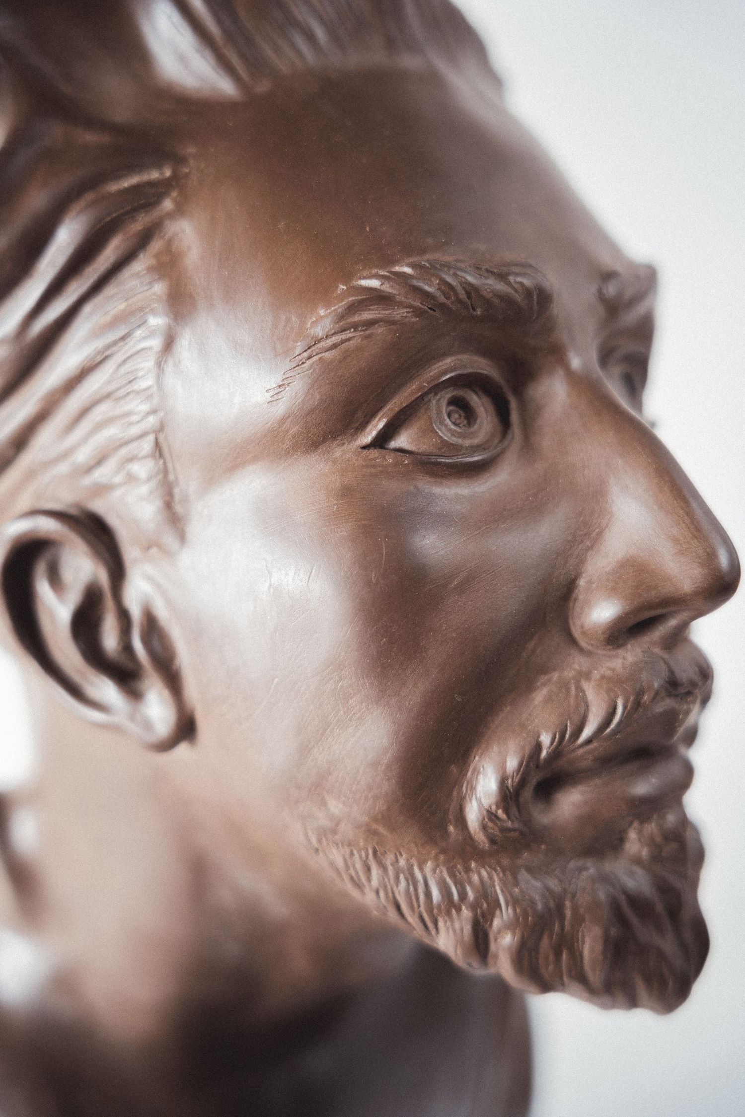 Detailed side profile of a bronze bust sculpture depicting a bearded man with realistic facial features.