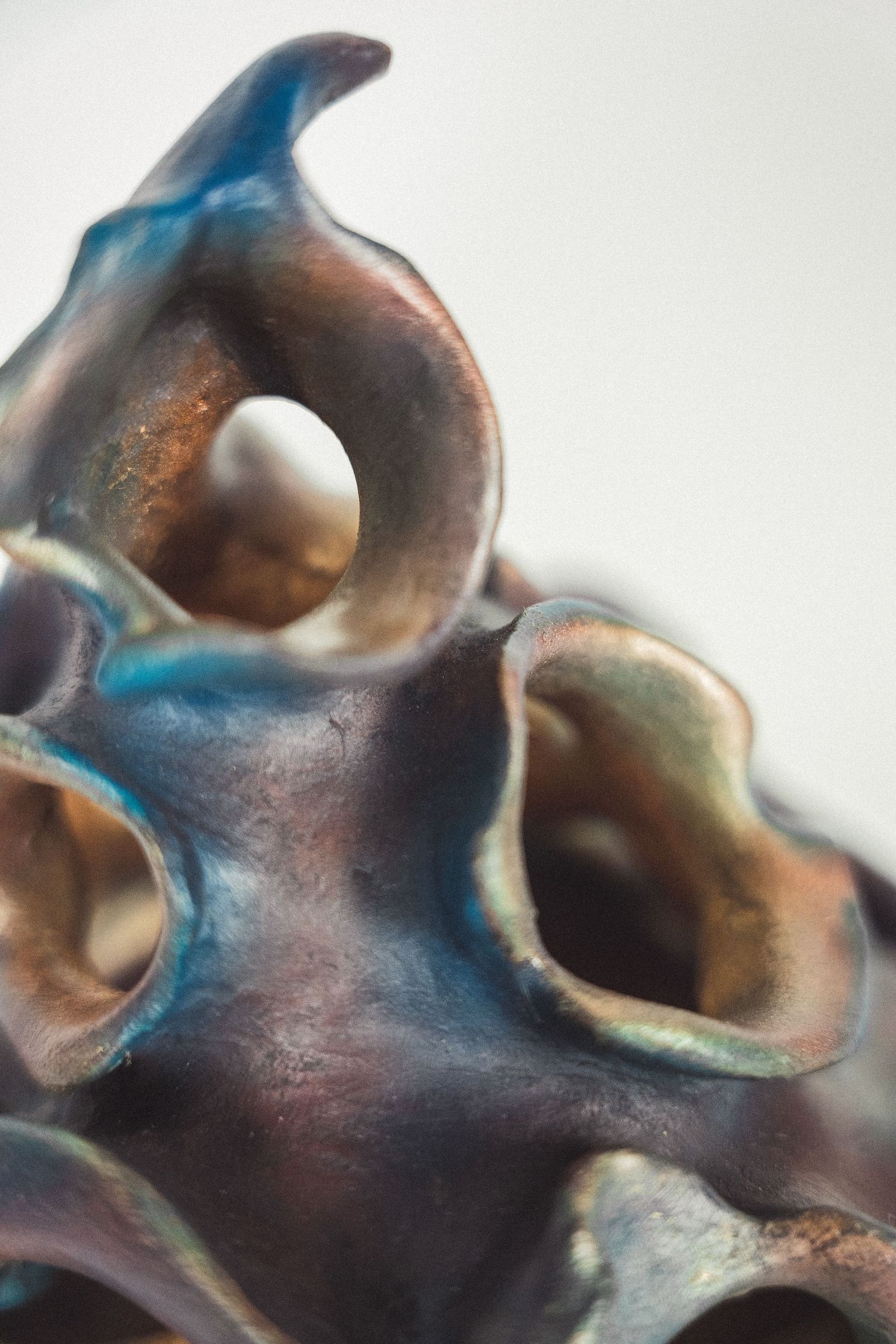 Detail of a raku-fired ceramic sculpture featuring iridescent blue-copper glazed organic hollow forms.