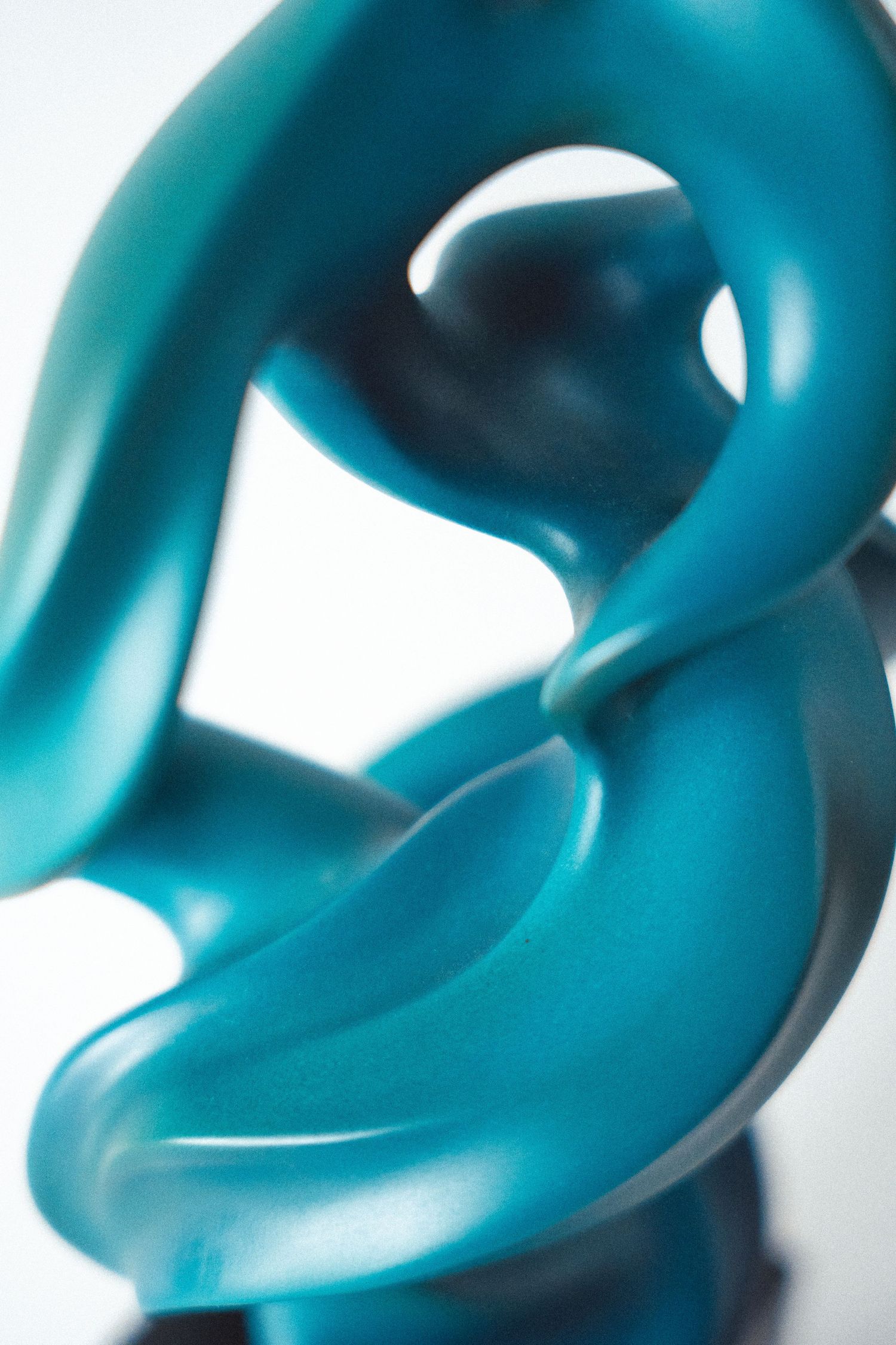 Abstract teal blue frosted glass sculpture with smooth flowing curves and organic twisted form on white background.