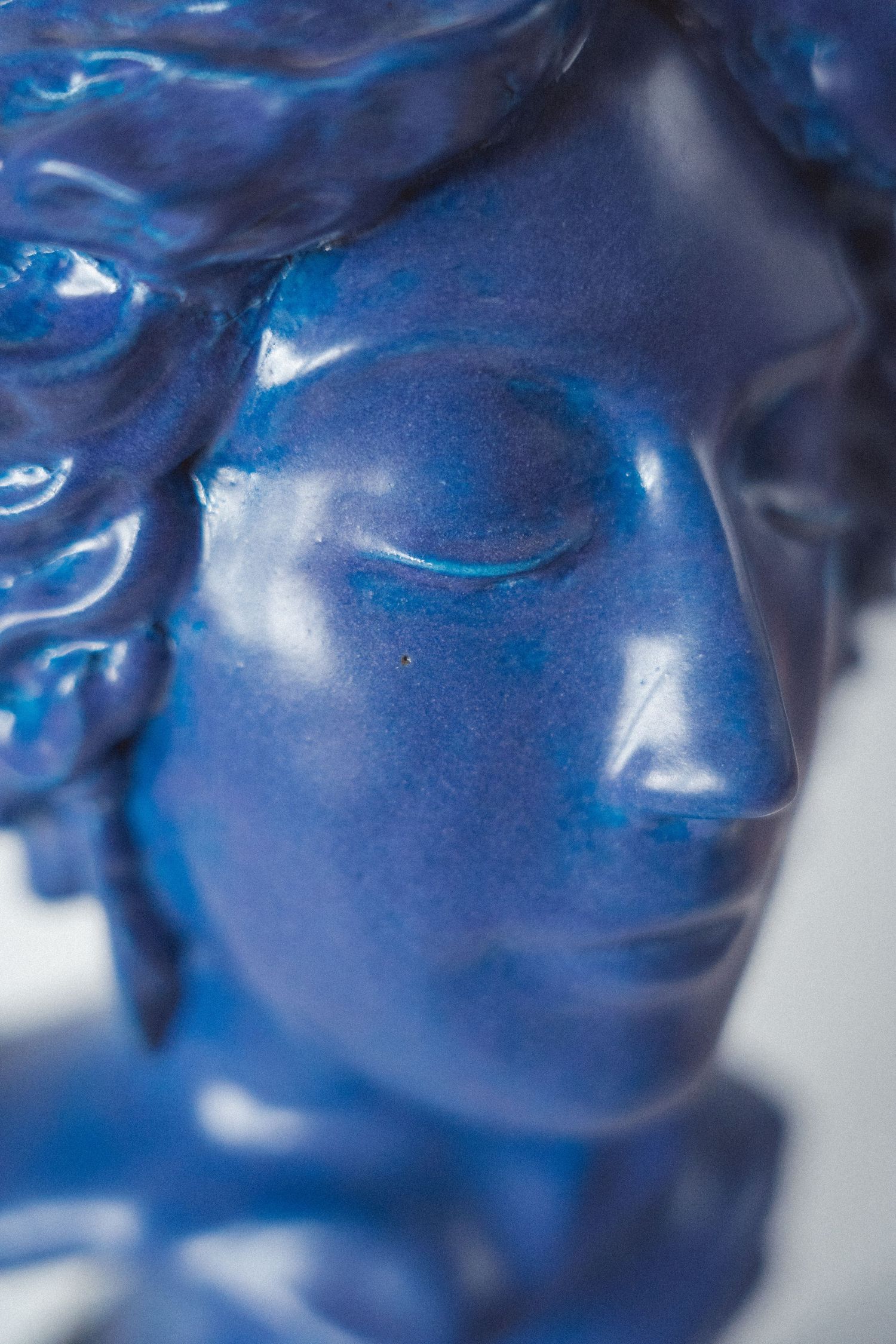 Close-up of a glossy blue ceramic classical bust sculpture with closed eyes.