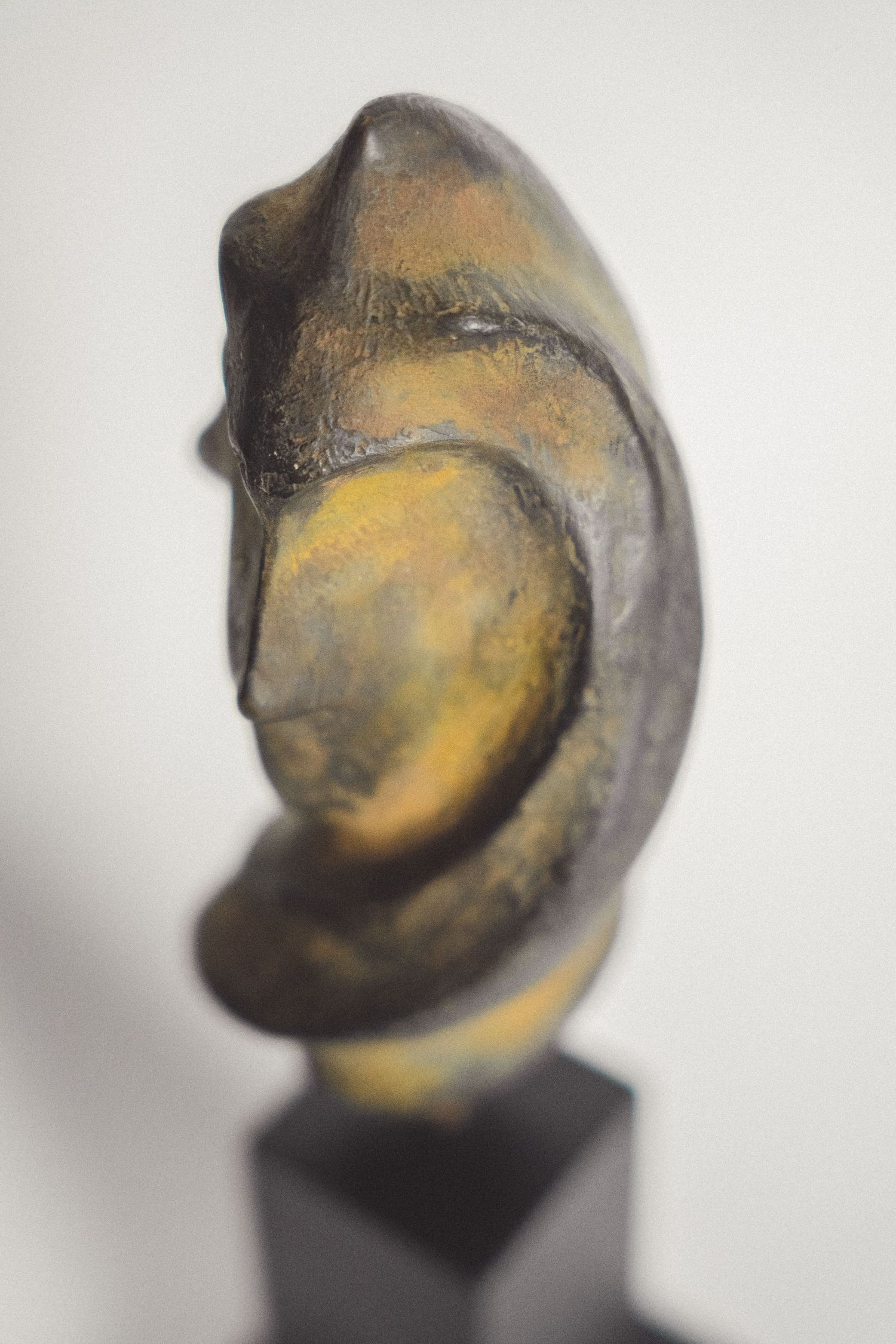 Abstract bronze sculpture with golden and dark patina on black base, depicting a stylized human face in profile.