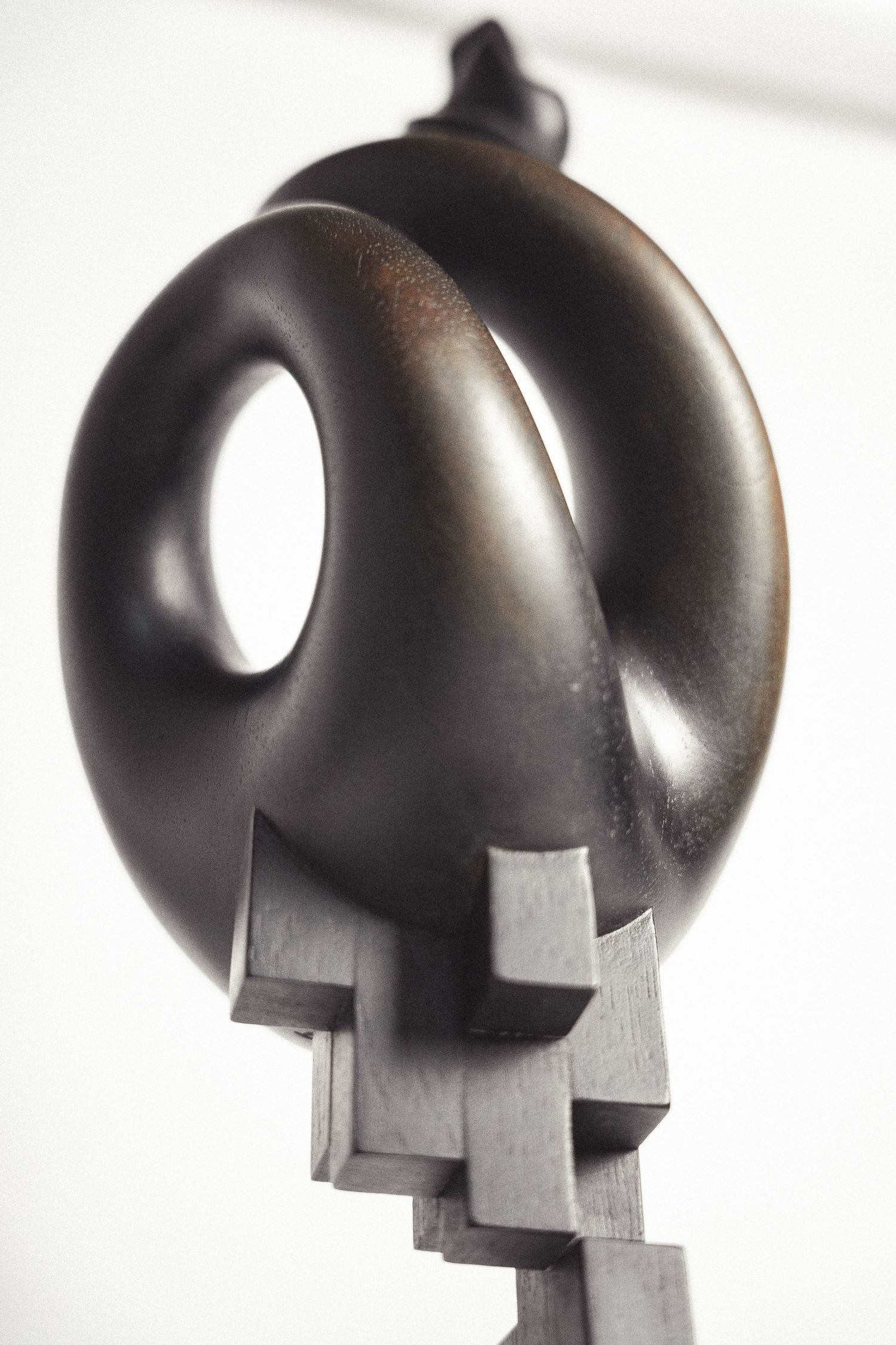 Close-up of dark bronze abstract sculpture featuring smooth toroidal form on geometric cubic pedestal.