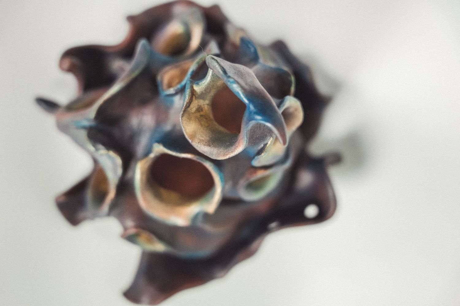 Top-down view of an abstract ceramic sculpture with iridescent dark blue and bronze raku-fired glaze.