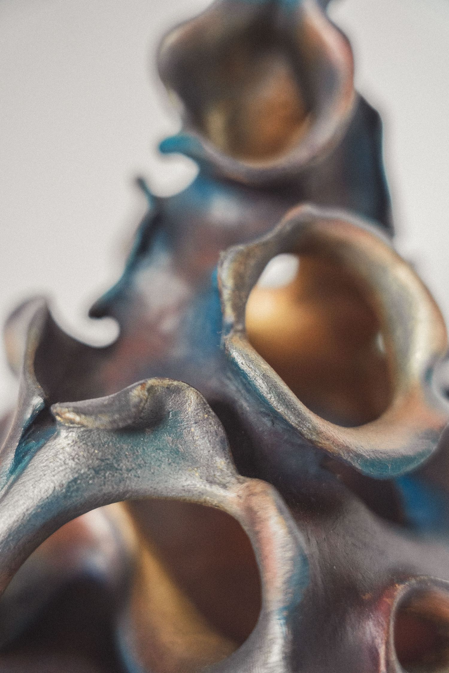 Close-up of an abstract ceramic sculpture with iridescent blue and bronze glazed organic openings.