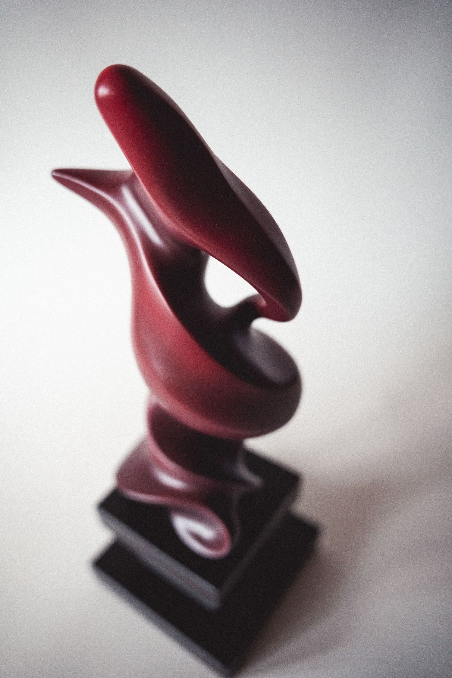 Dark red abstract sculpture with flowing curved forms mounted on a black base.