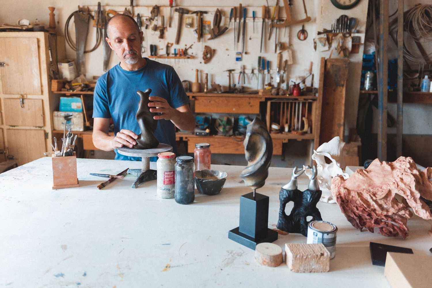 Male sculptor working in a rustic workshop surrounded by tools and various sculptures.
