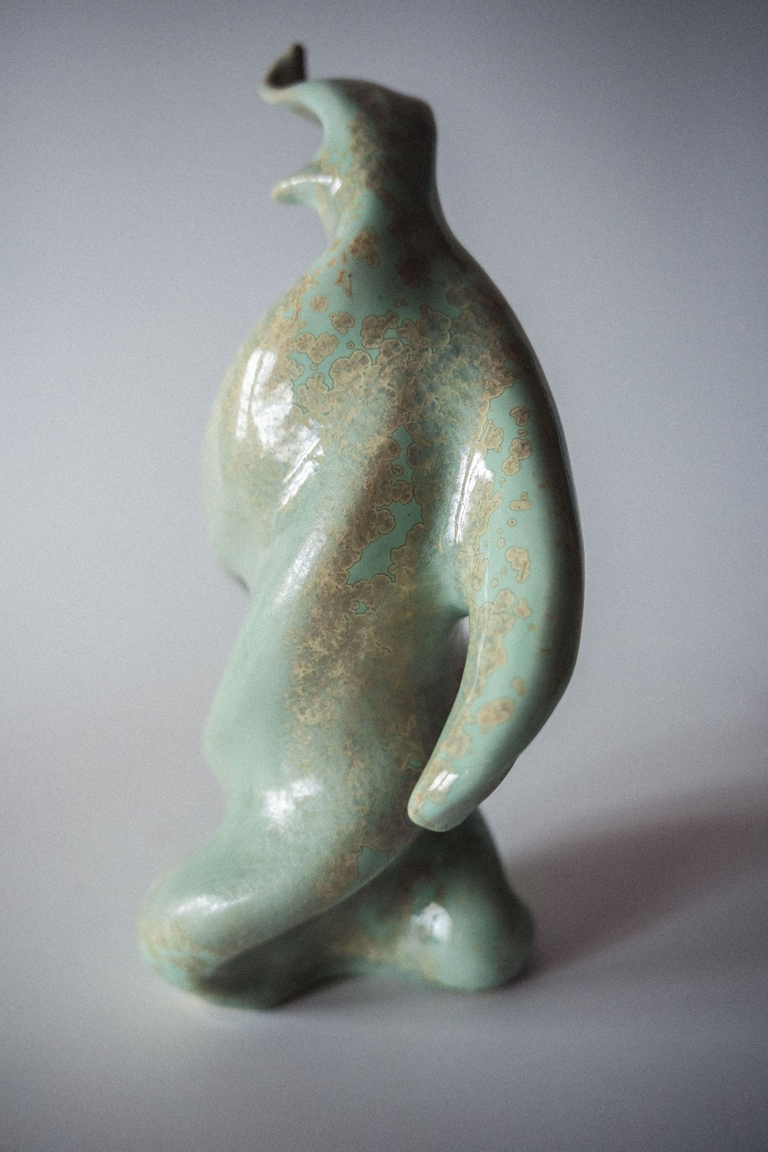 Handmade ceramic penguin figurine with a matte celadon green glaze and rustic brown speckles.