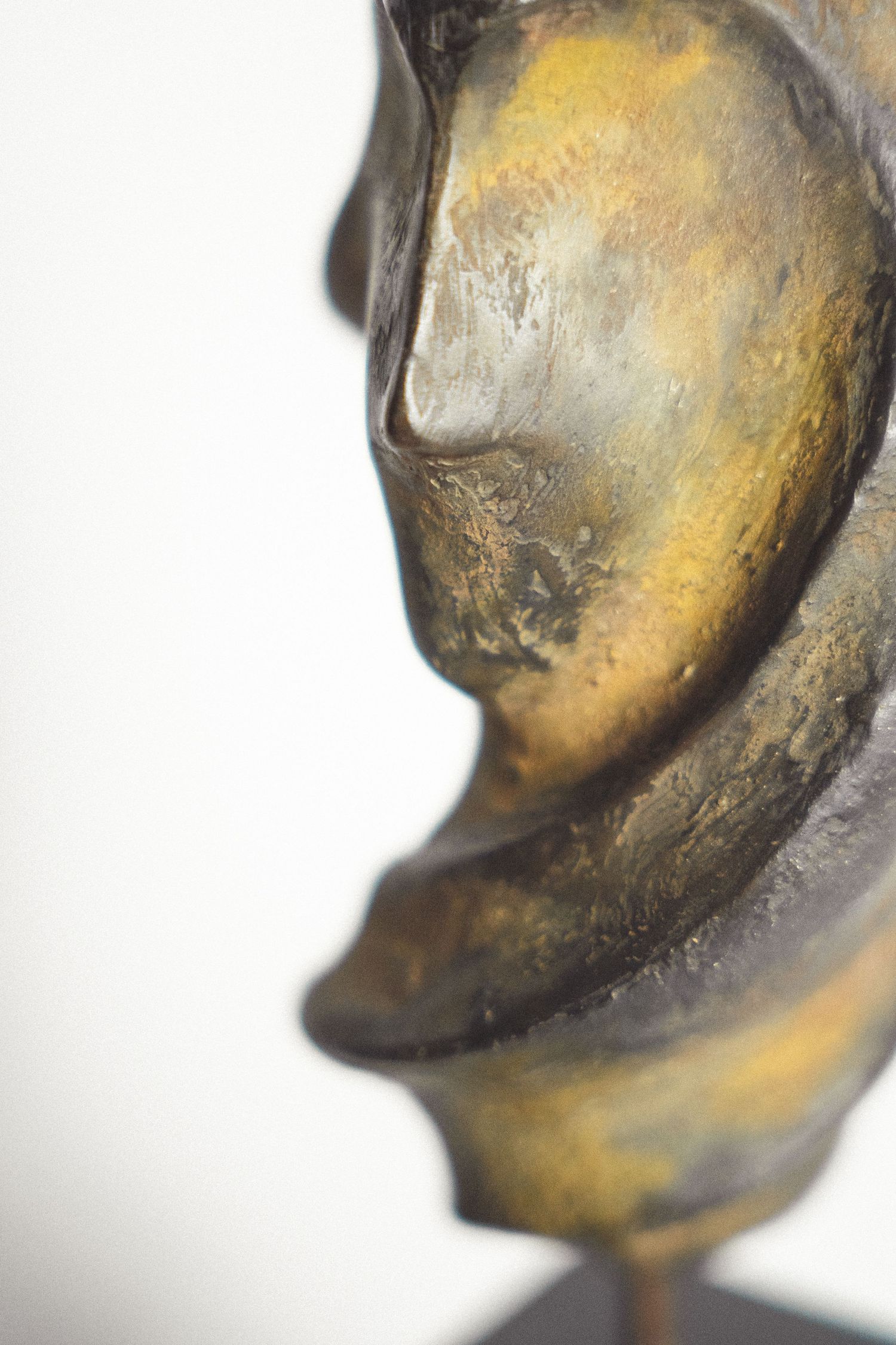 Close-up of a bronze Buddha sculpture with golden patina, showing serene facial profile against white background.