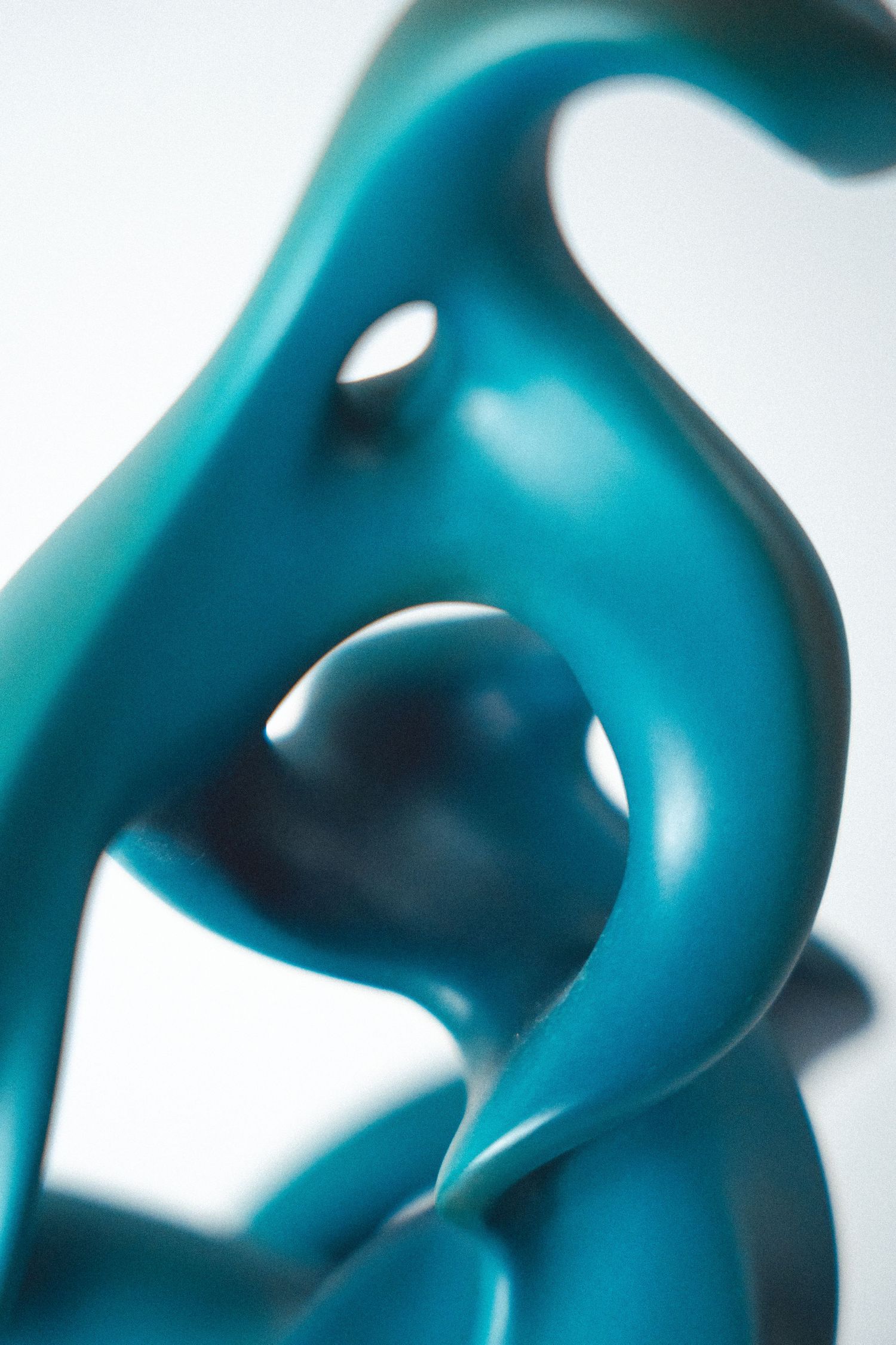 Close-up of a teal abstract sculpture with smooth curves and organic flowing shapes on a white background.