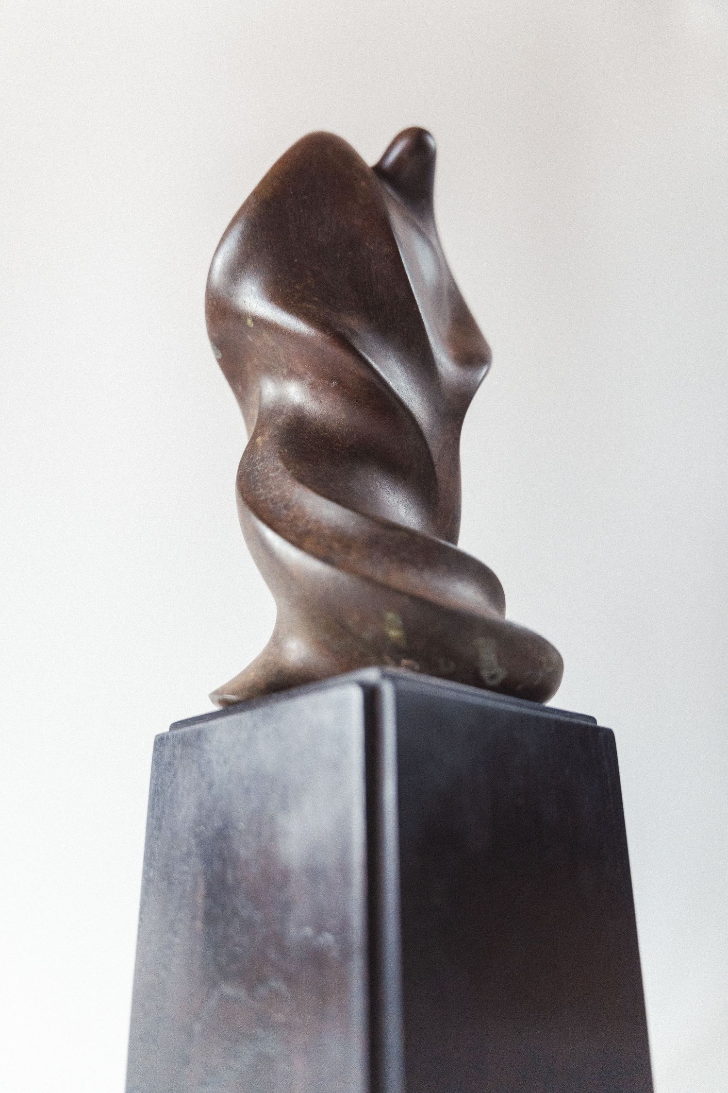 Dark bronze abstract figurative sculpture with twisted spiral form mounted on a black pedestal.