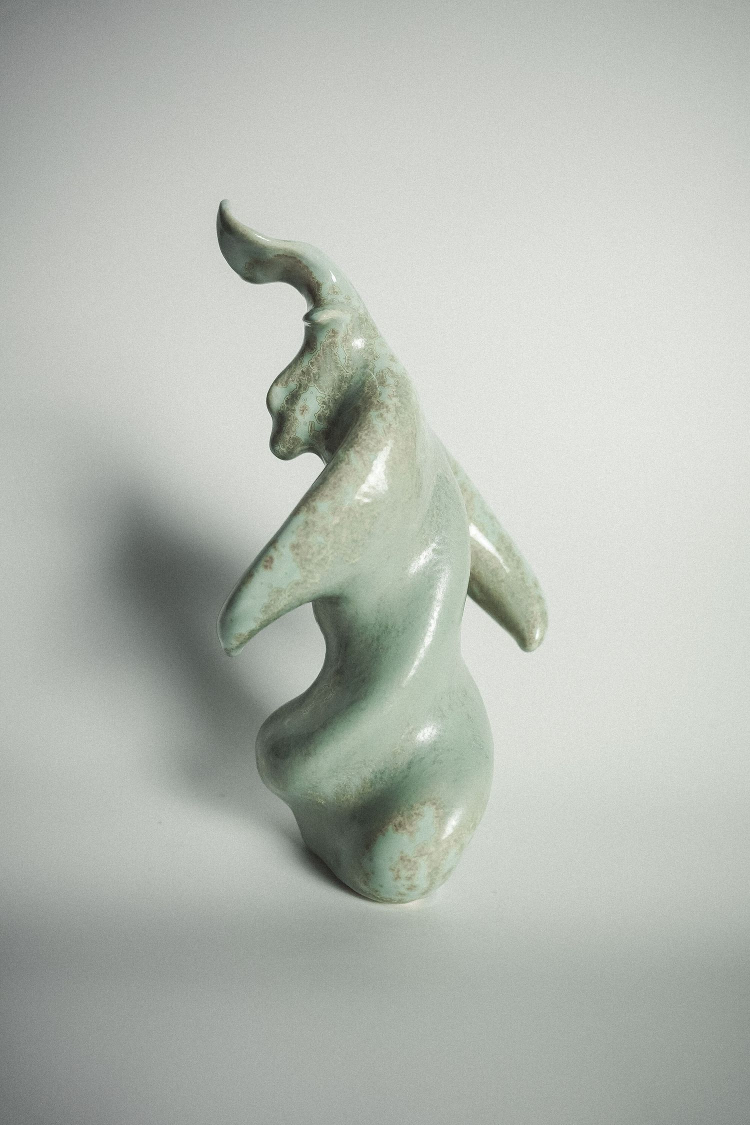 Abstract ceramic figurine with celadon green glaze depicting a stylized dancing animal form.