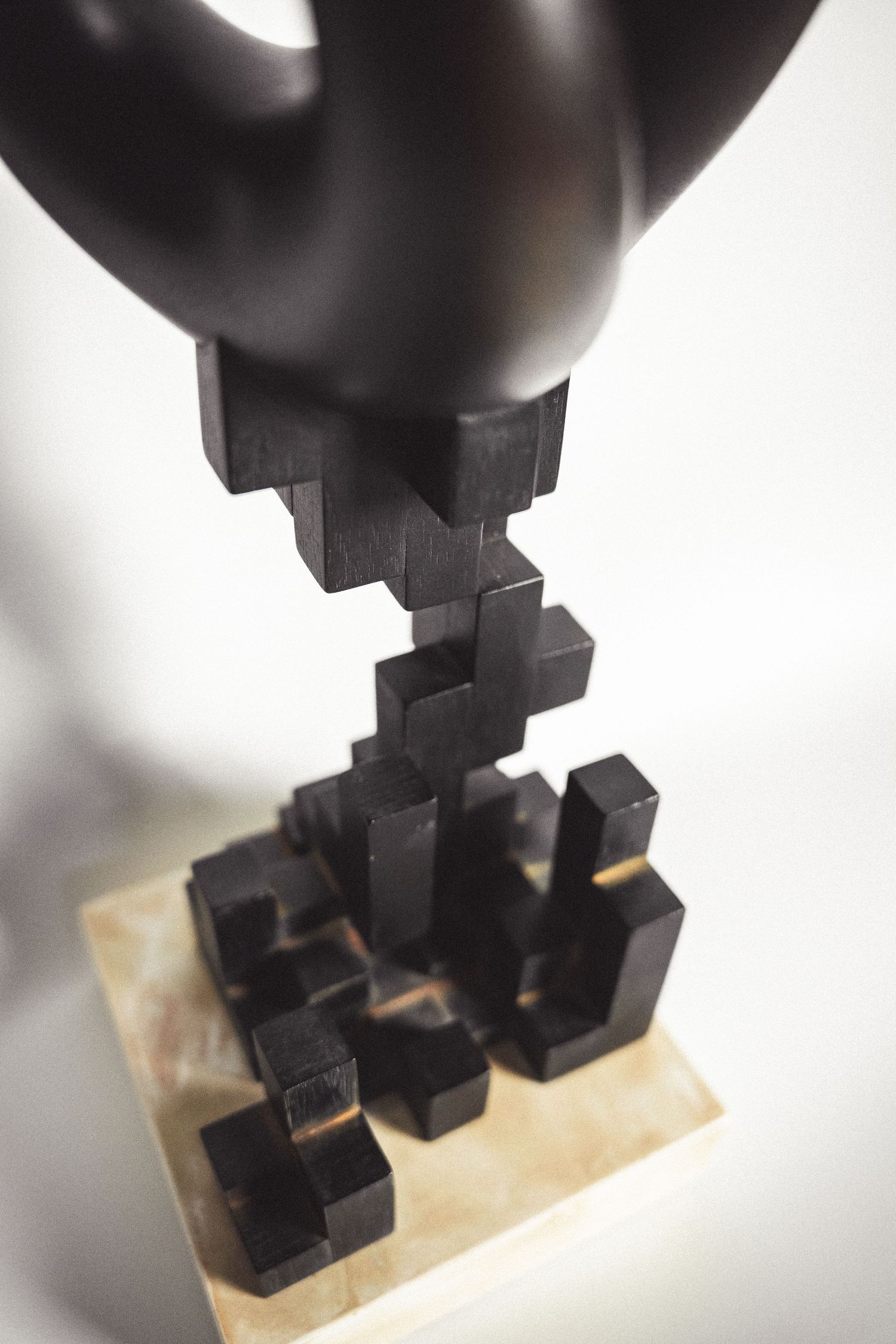 Detail of dark geometric cubic base of abstract bronze sculpture on light marble platform.