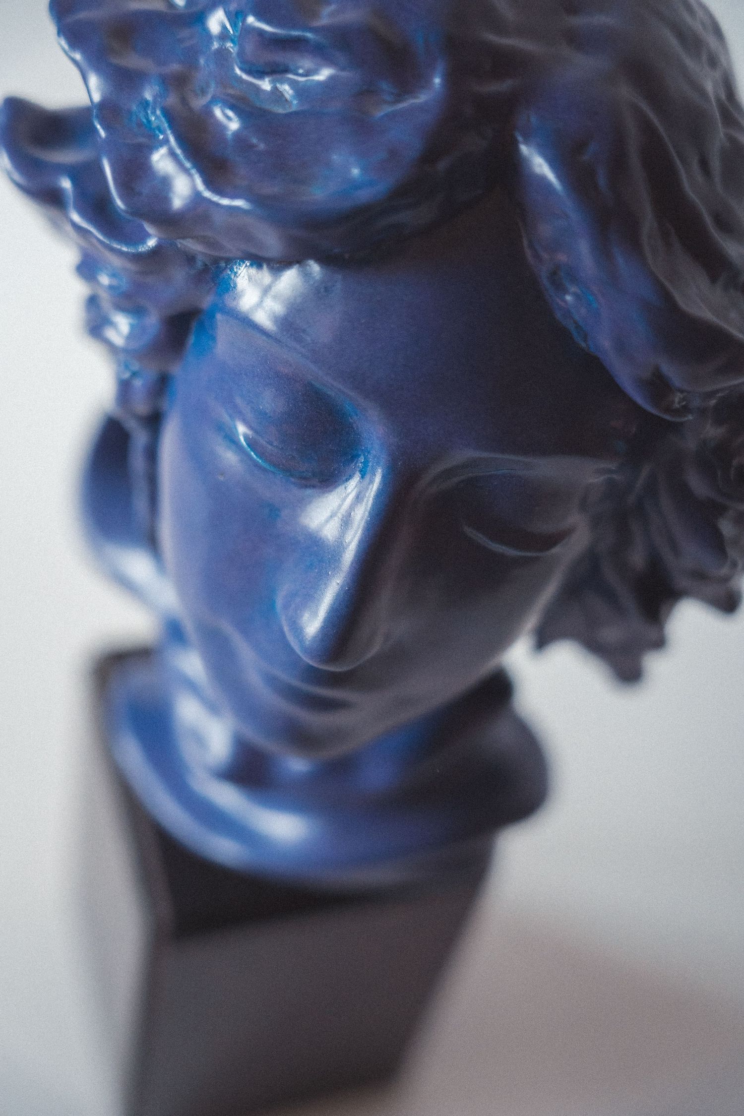 Glossy deep blue bust sculpture of a classical figure with flowing hair on dark base.