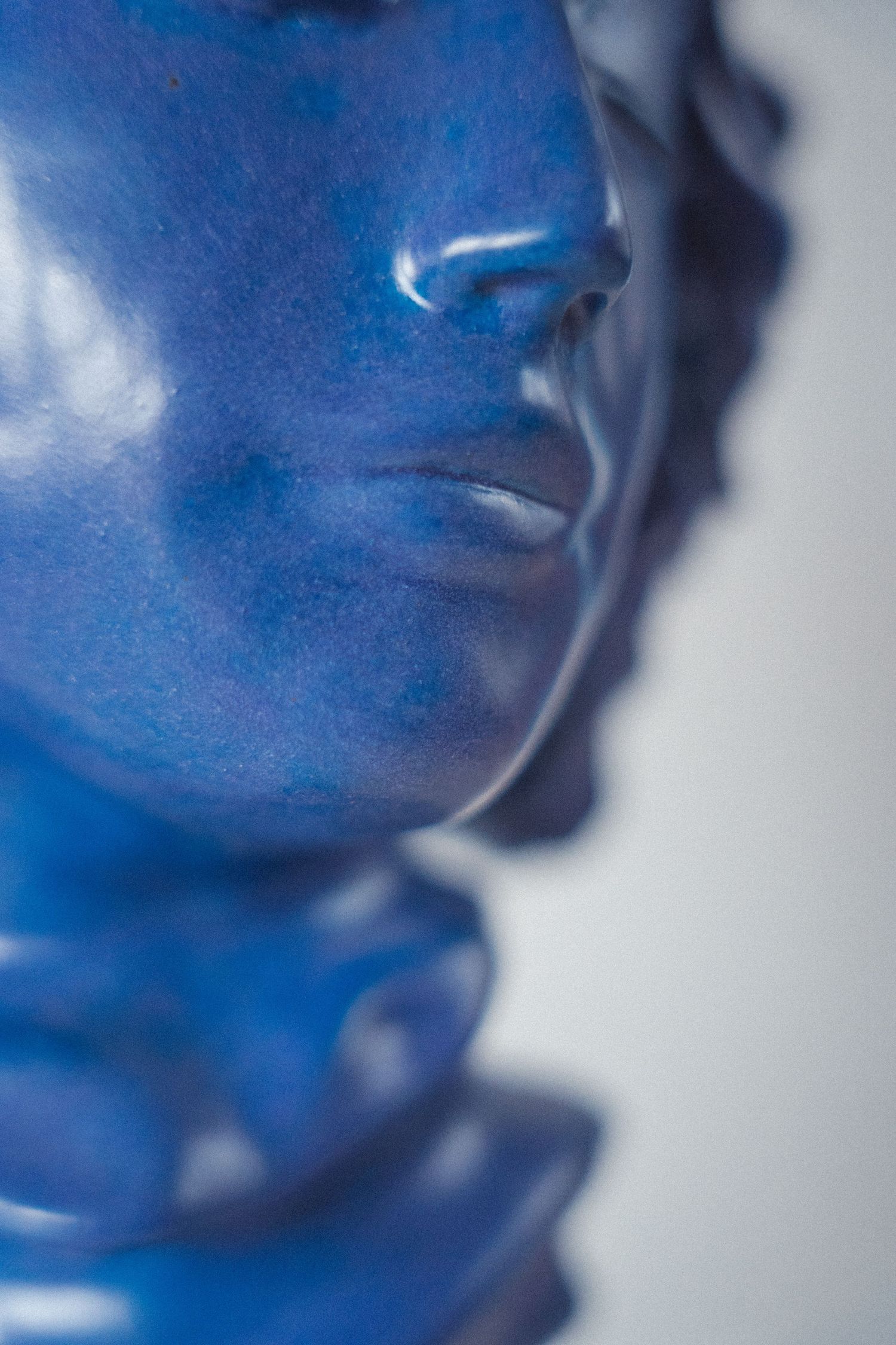 Side profile close-up of a matte blue ceramic classical bust sculpture.