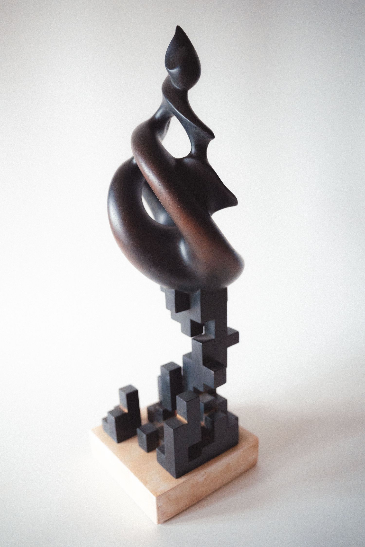 Dark bronze abstract sculpture with organic twisting forms on stepped geometric cubic wooden base.