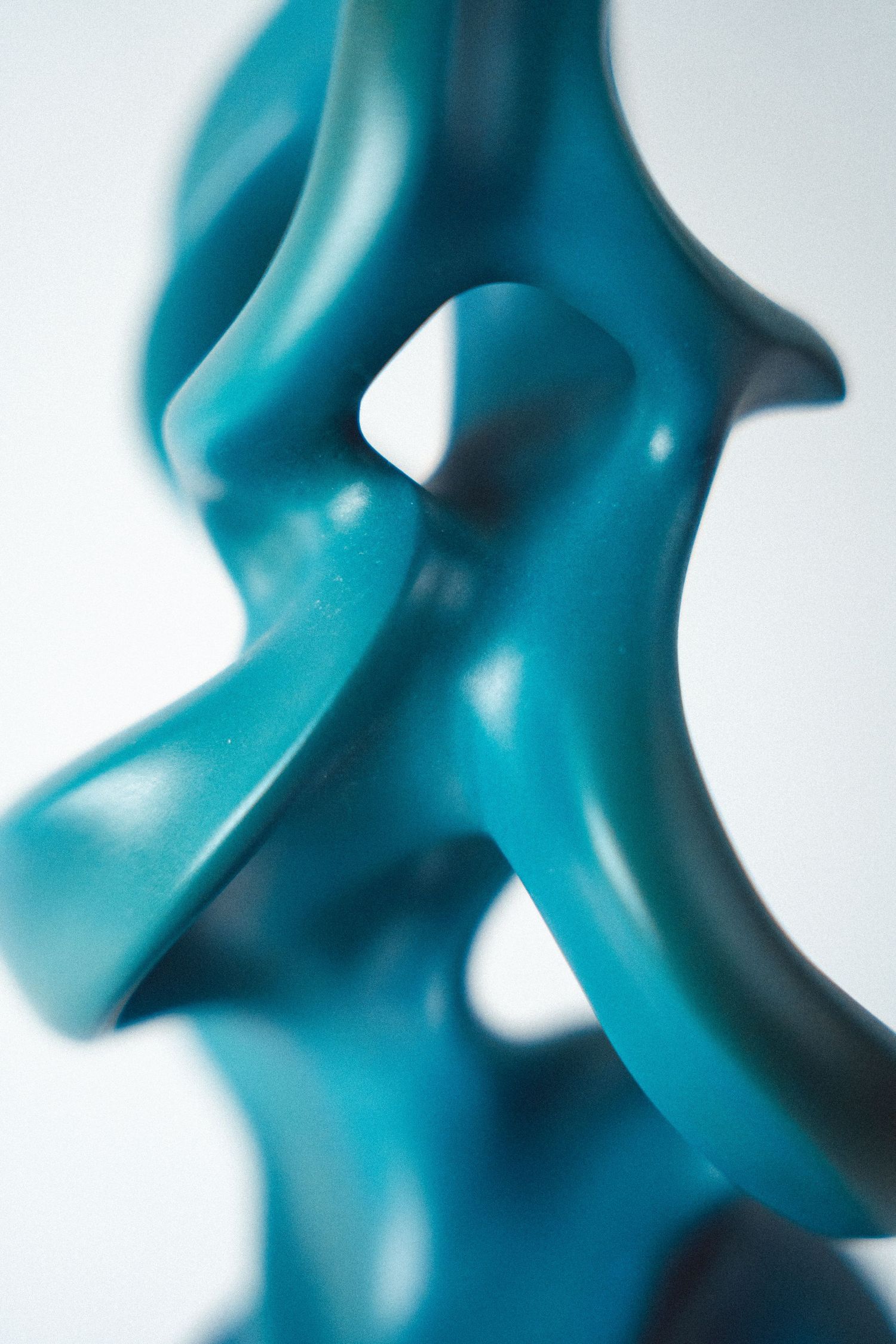Close-up of a teal abstract sculpture with flowing, intertwined curves against a white background.