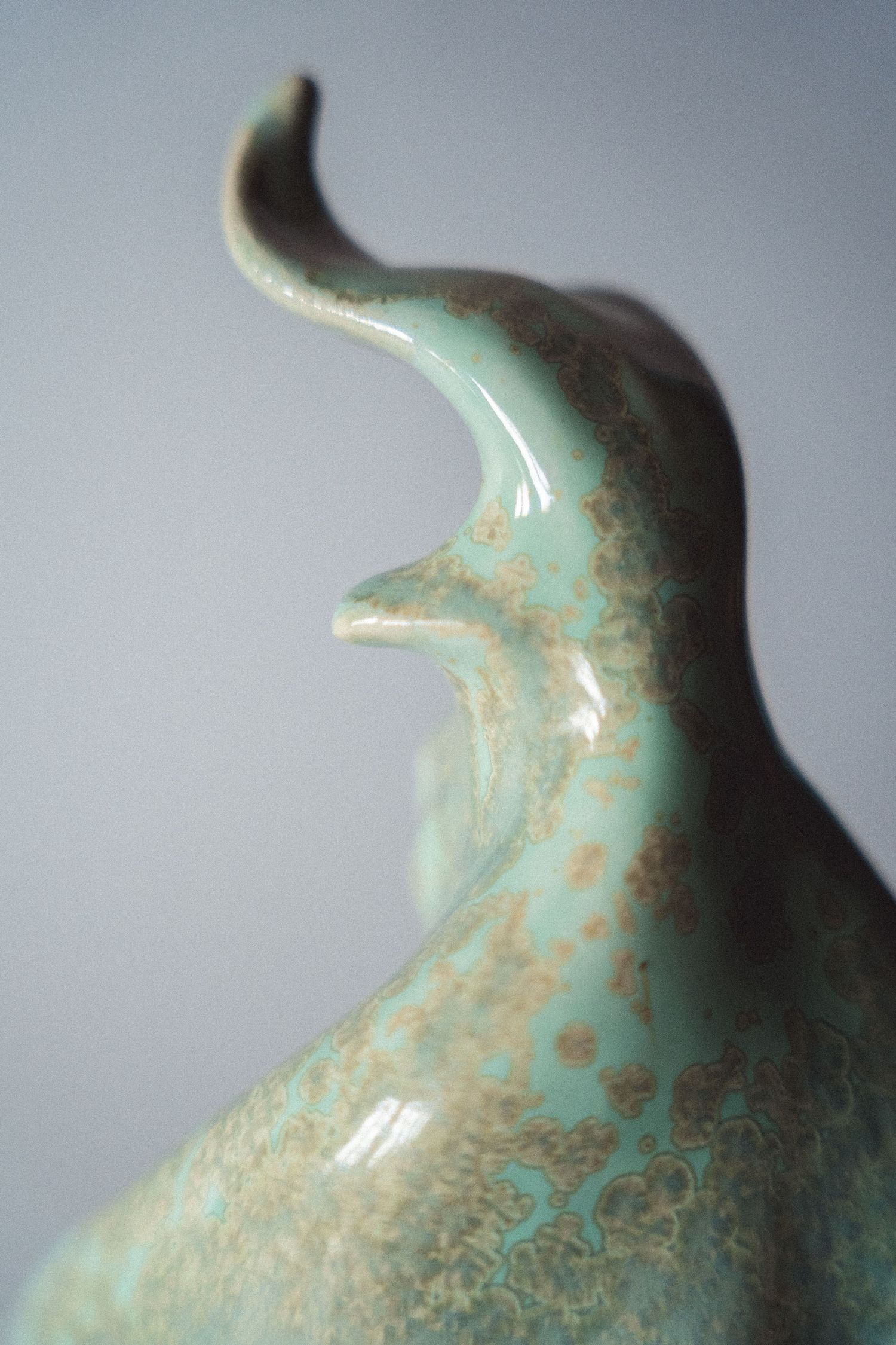 Close-up of a ceramic sculpture tip with a curved horn detail in speckled mint green glaze.
