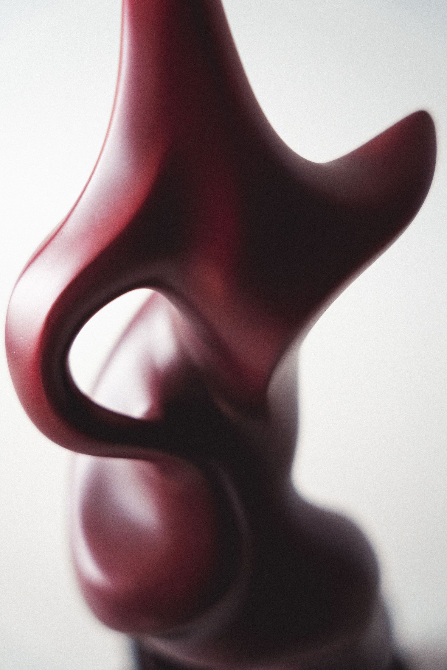 Close-up detail of a smooth dark red abstract sculpture with flowing curved forms.