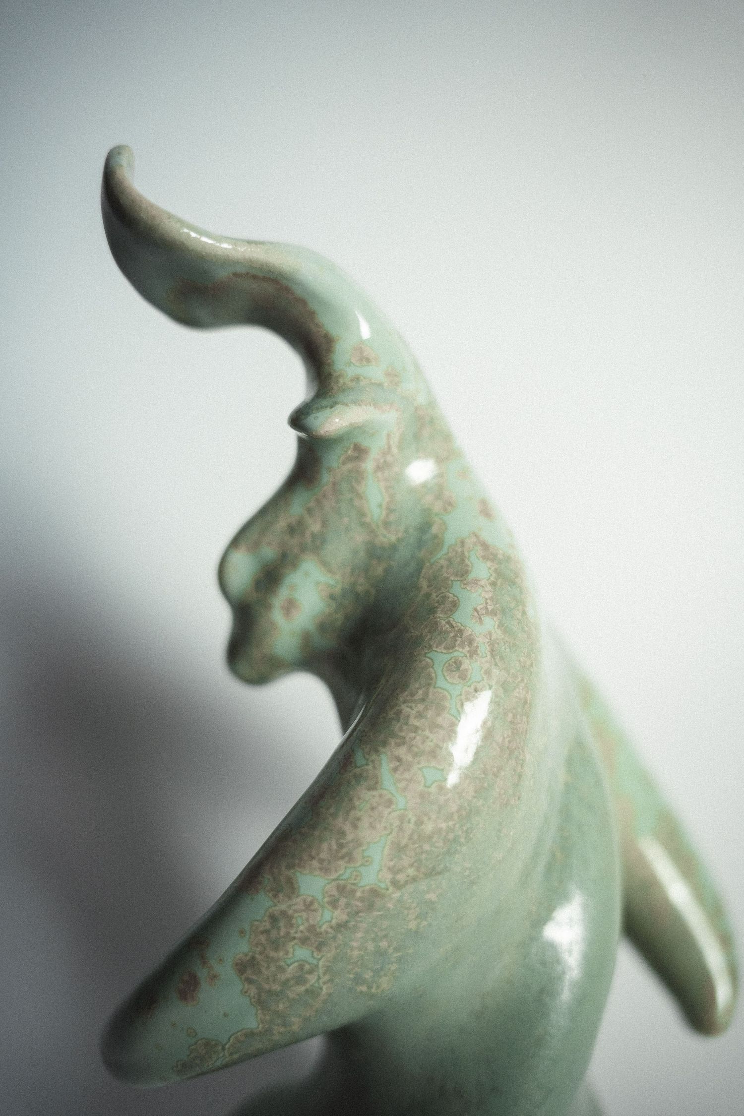 Close-up of a green ceramic bull figurine with speckled glaze and curved horns.