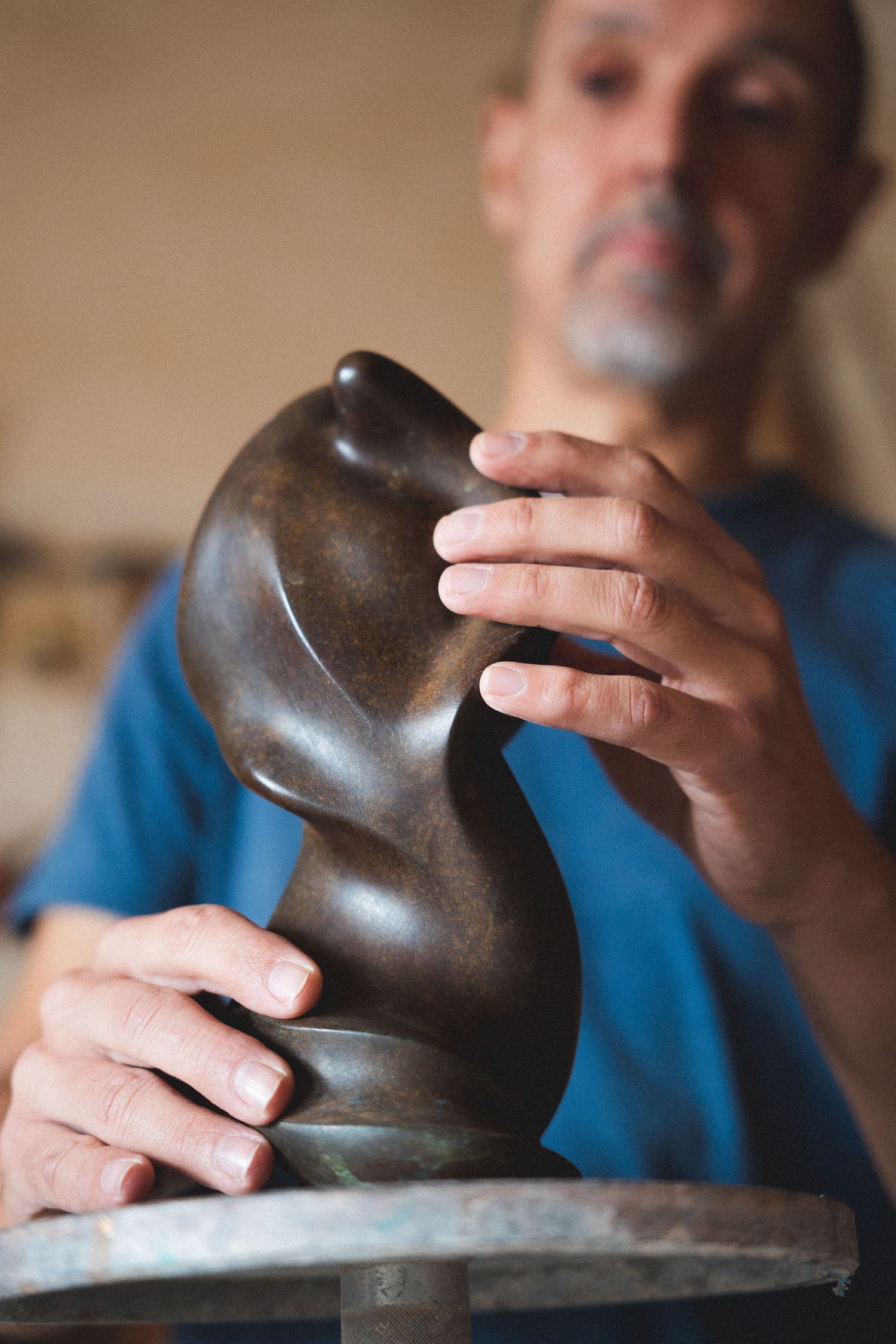 Artist carefully examining a small dark abstract sculpture with both hands in studio.