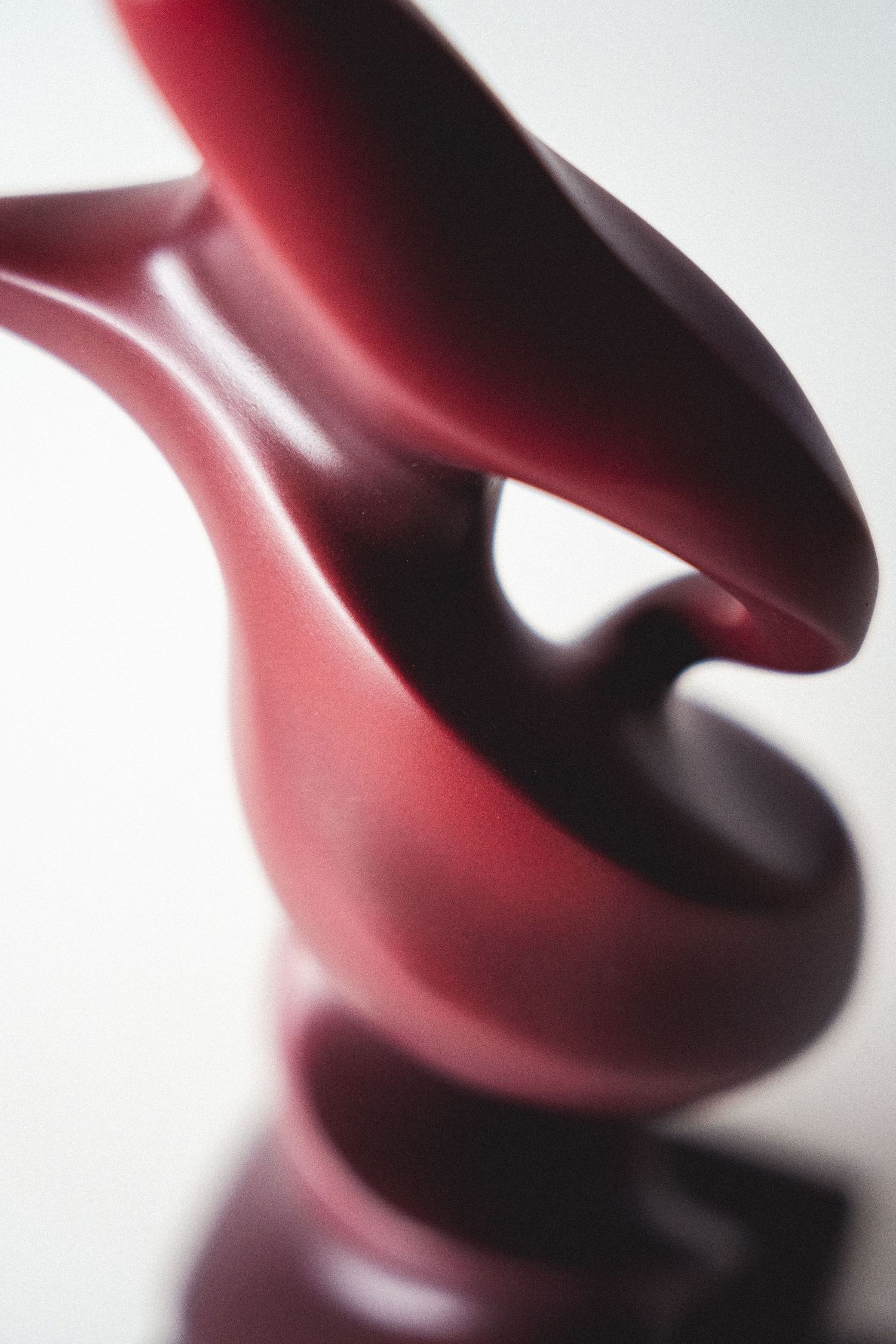 Abstract dark red polished sculpture with smooth curved forms on a reflective surface.