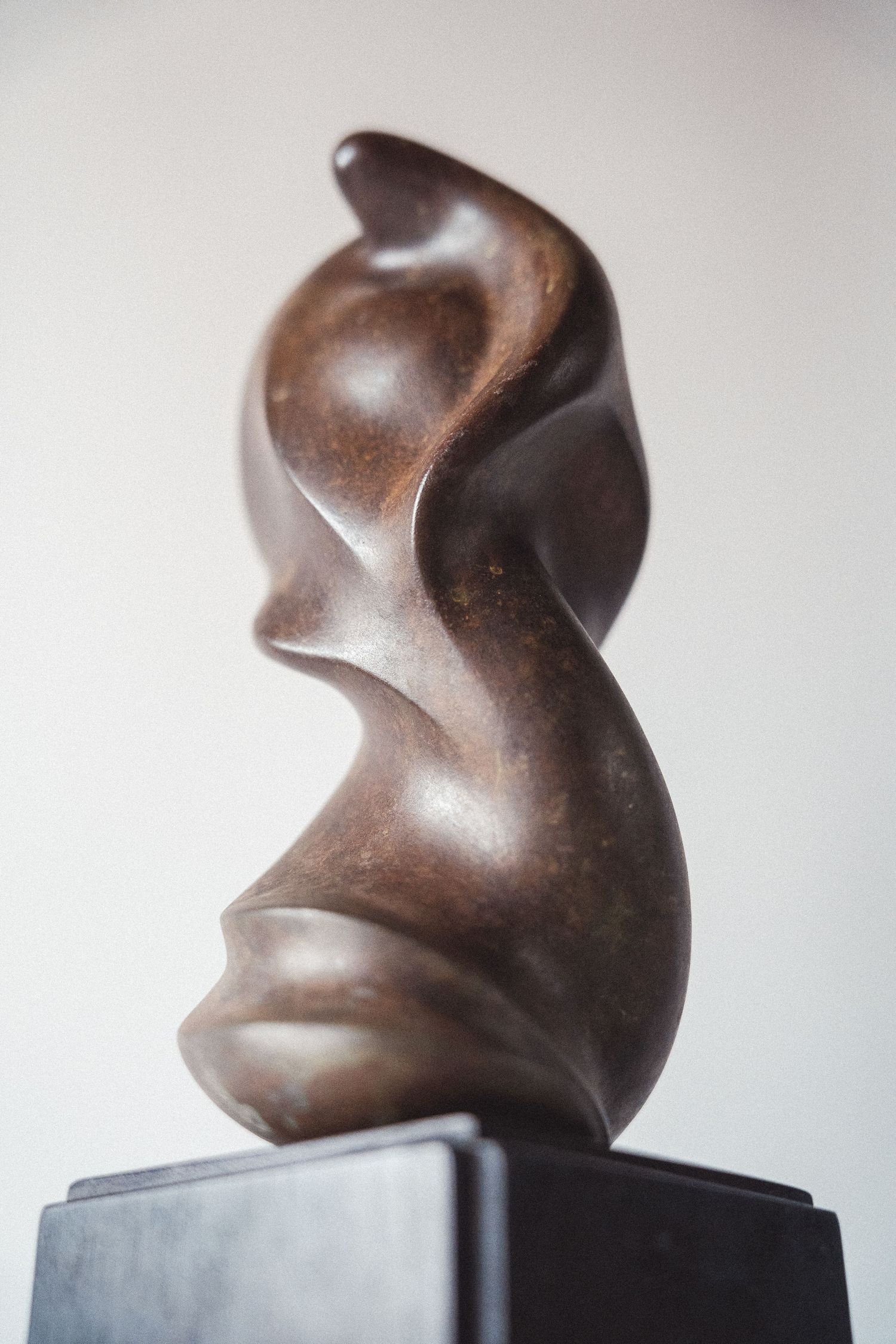 Abstract bronze sculpture with flowing organic curves suggesting a human figure on a dark base.