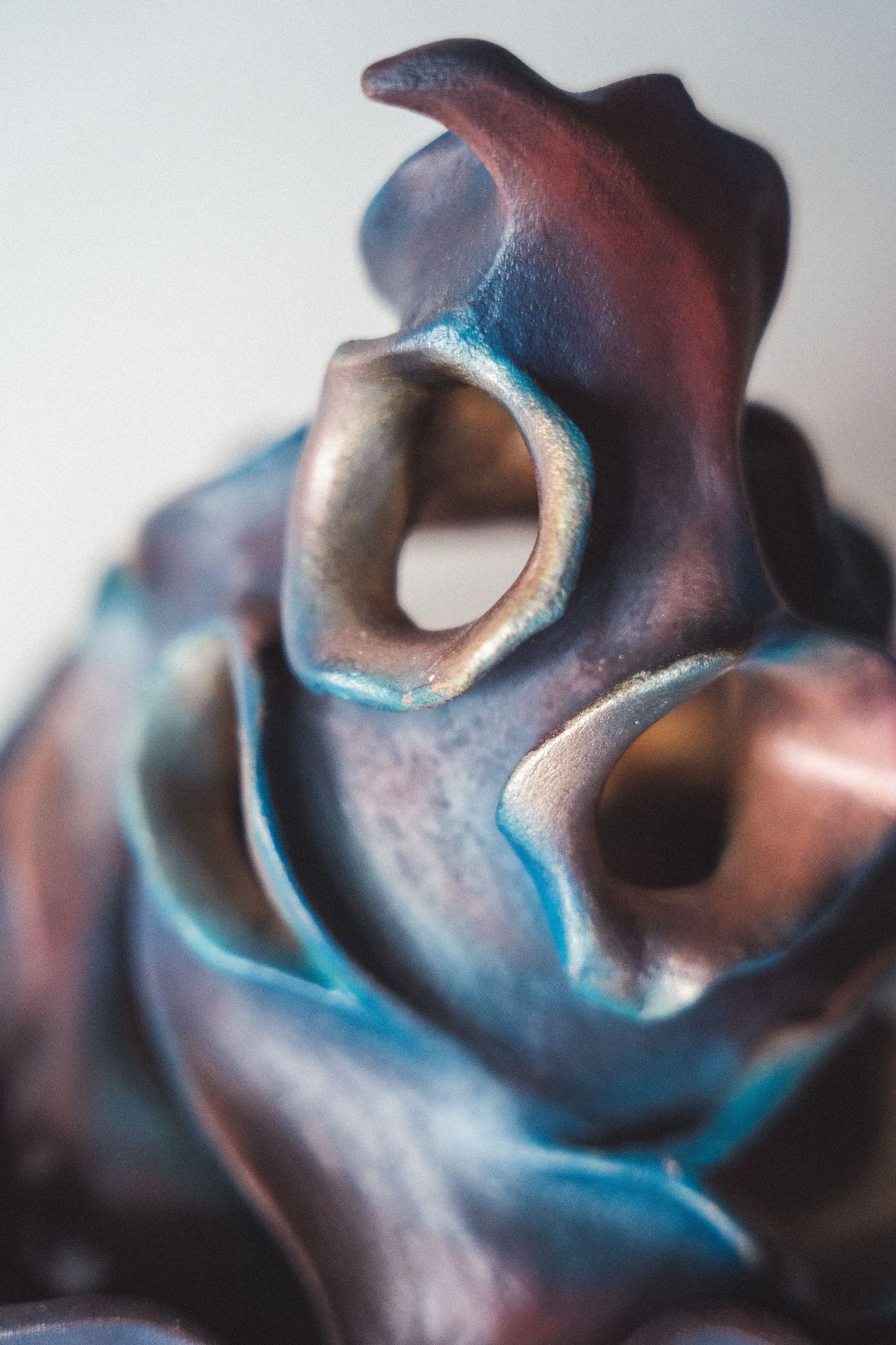 Close-up macro detail of an iridescent raku ceramic sculpture with blue and copper tubular openings.