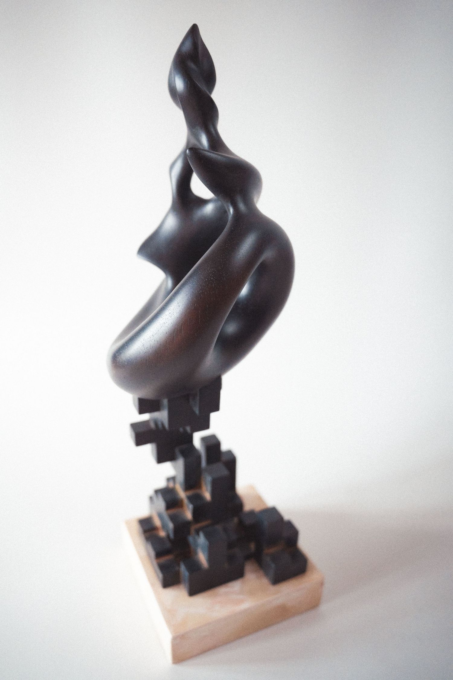 Dark bronze abstract sculpture featuring fluid organic shapes atop a geometric cubic wooden base.