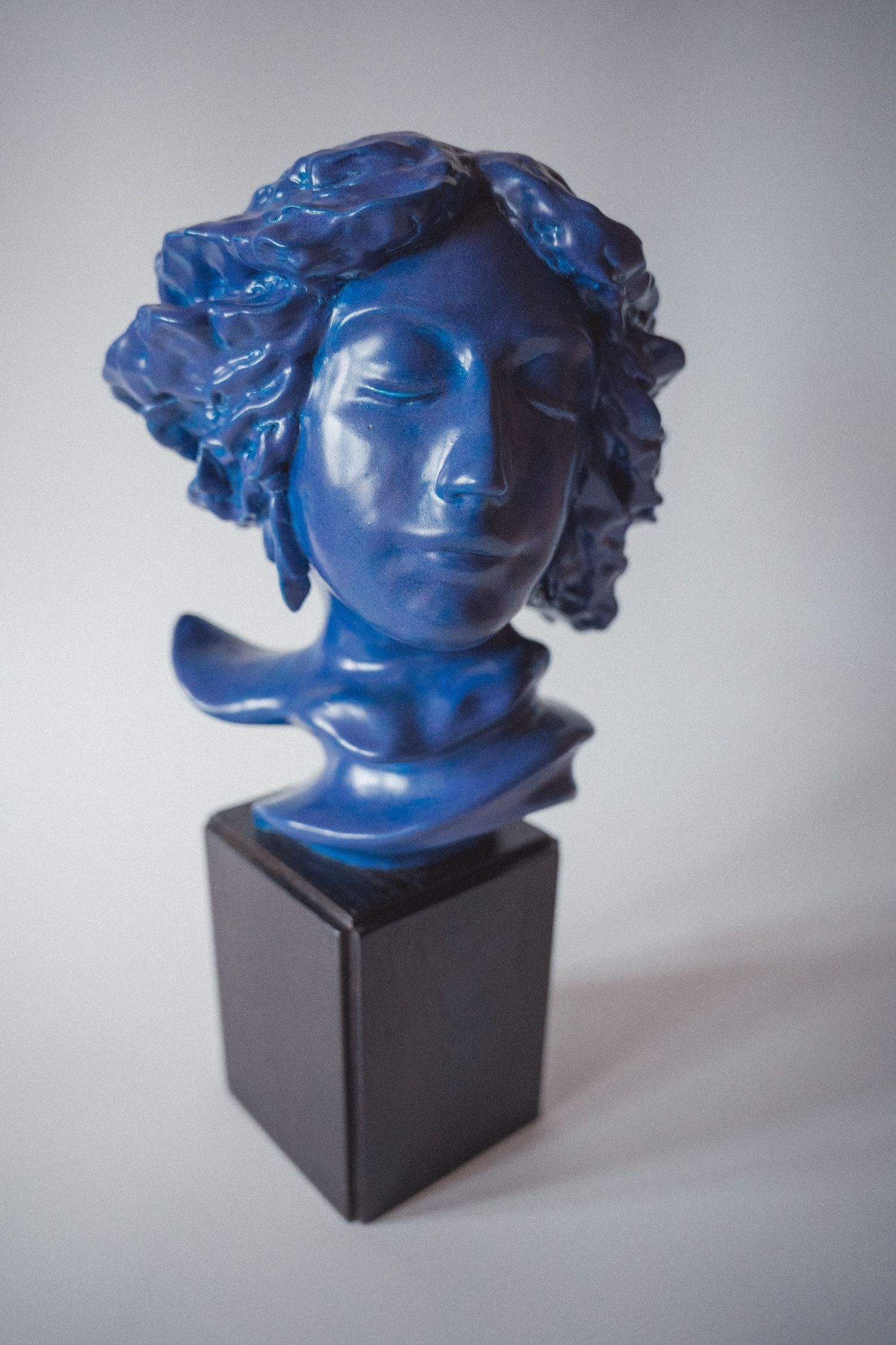 Blue resin bust sculpture of a classical female figure on a black pedestal.