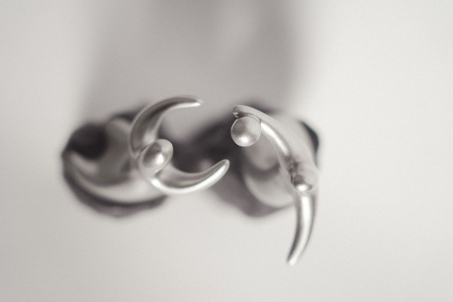 Close-up of silver crescent moon and spike charm earrings on a white background.