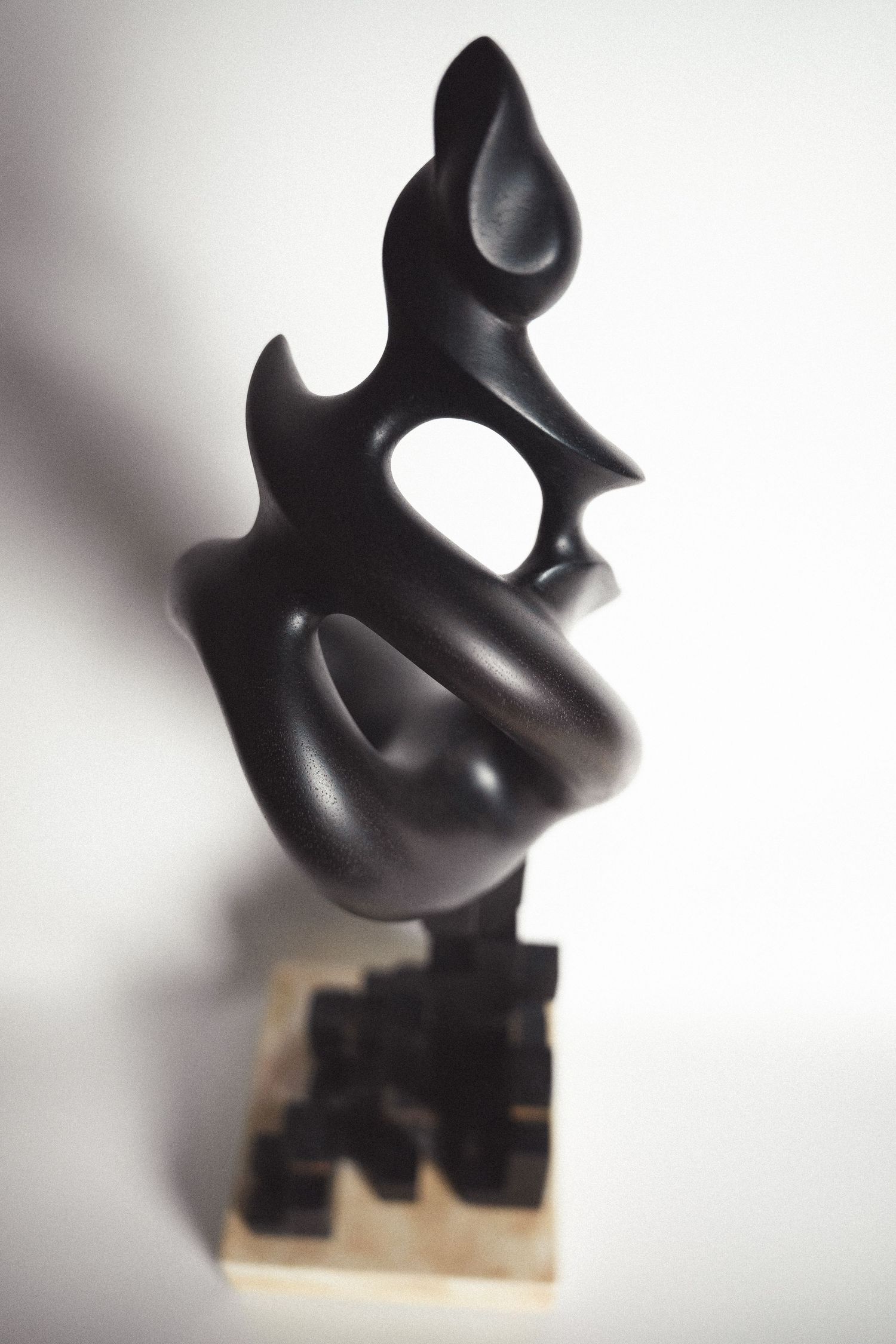 Dark abstract sculpture with flame-like organic forms and negative space on geometric cubic base.