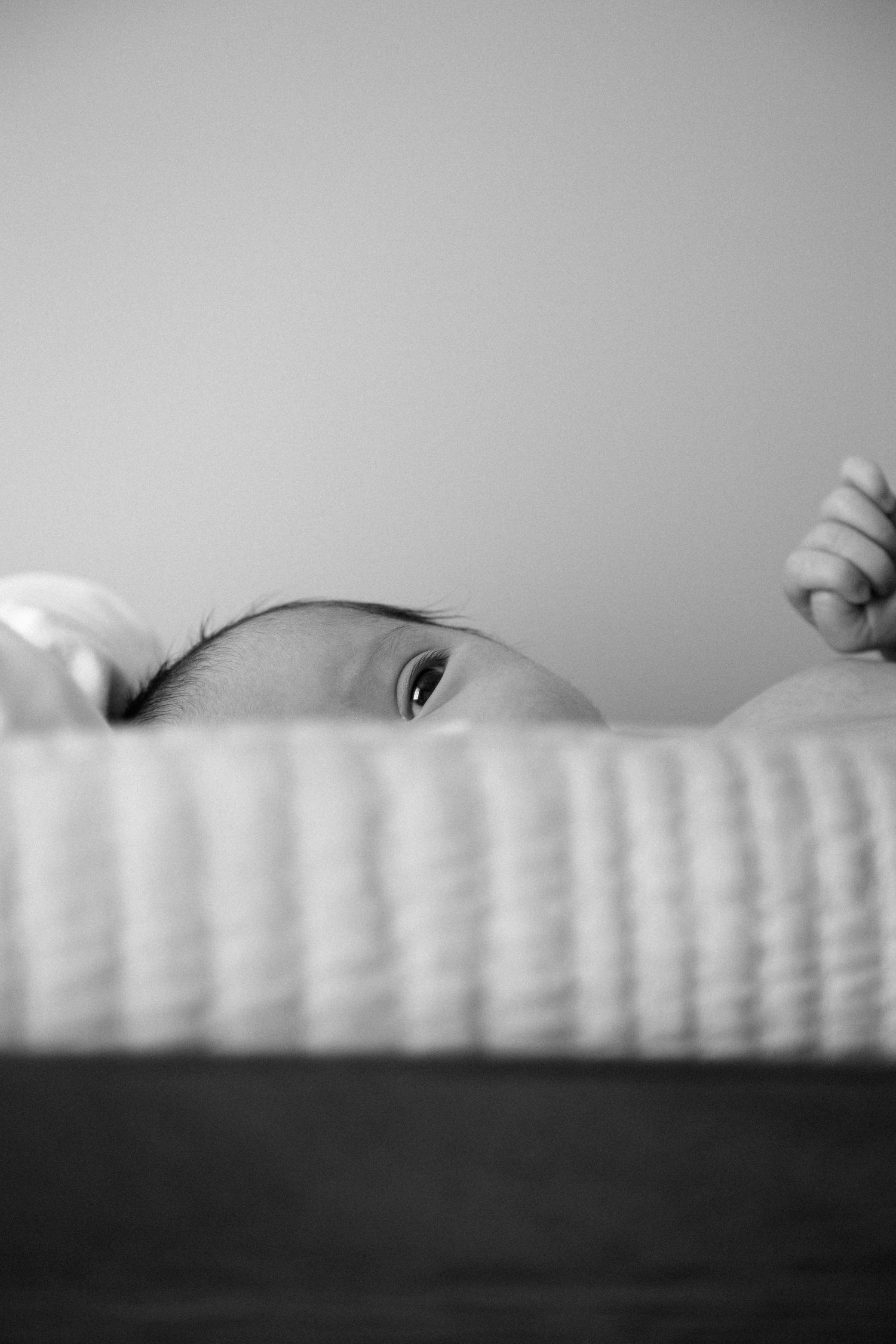 Newborn baby peering over edge of white wicker bassinet, black and white portrait photography.