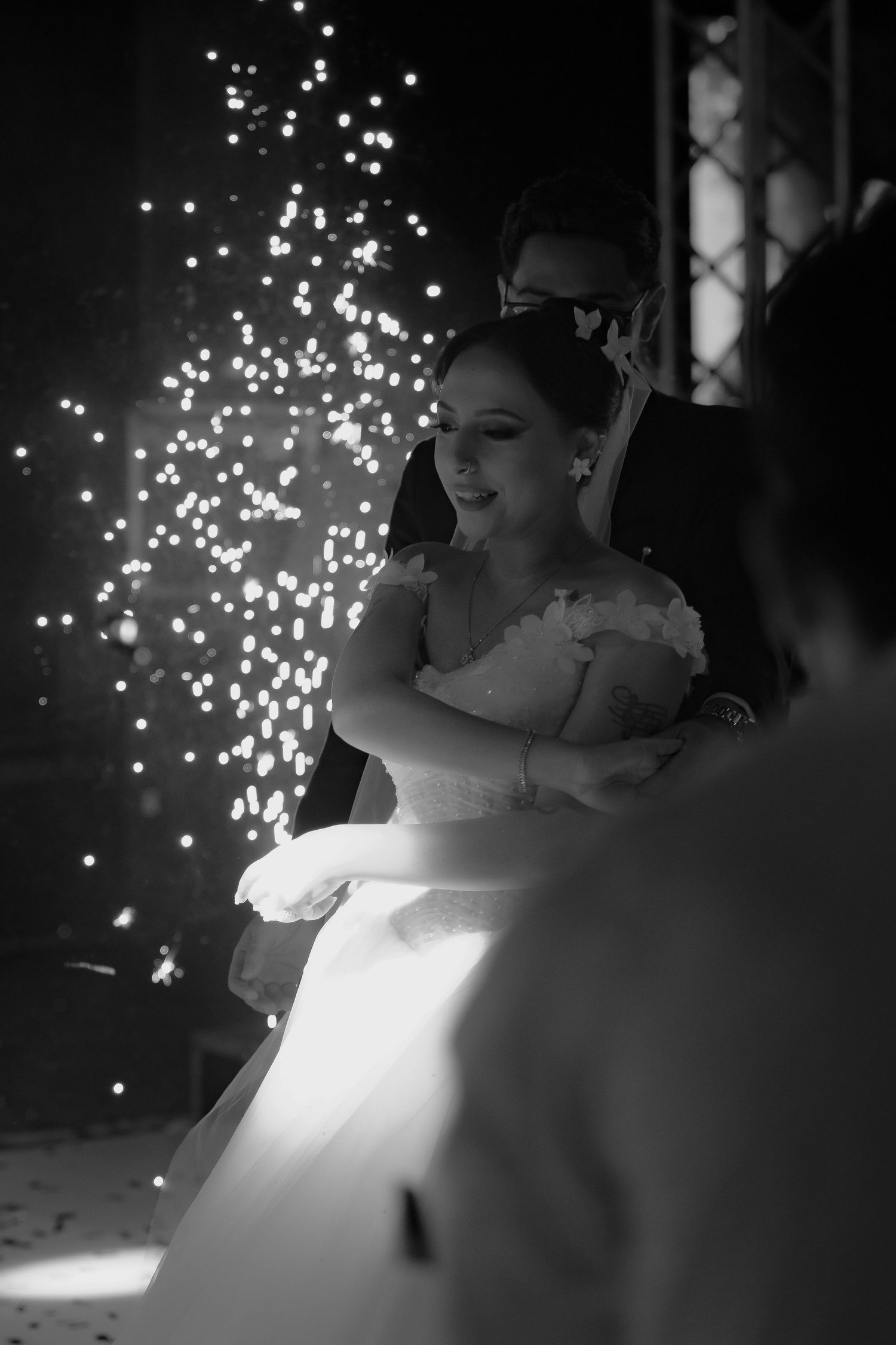 Black and white photo of smiling bride dancing with groom amid sparkling fireworks at elegant wedding reception.